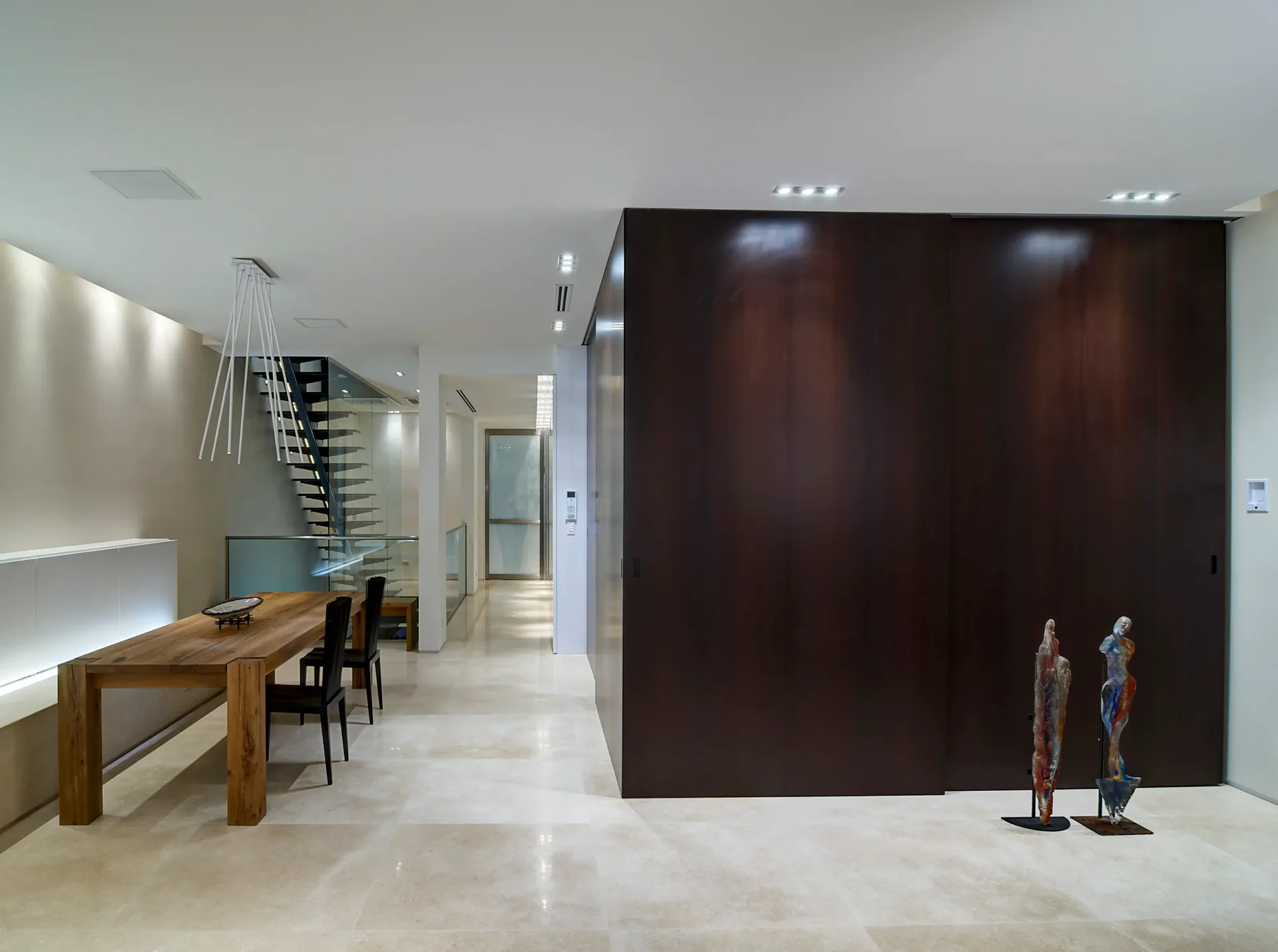 Modern gallery space with polished white floors, wooden reception desk, dark wood feature wall, and minimalist lighting design by Leopoldo Rosati.