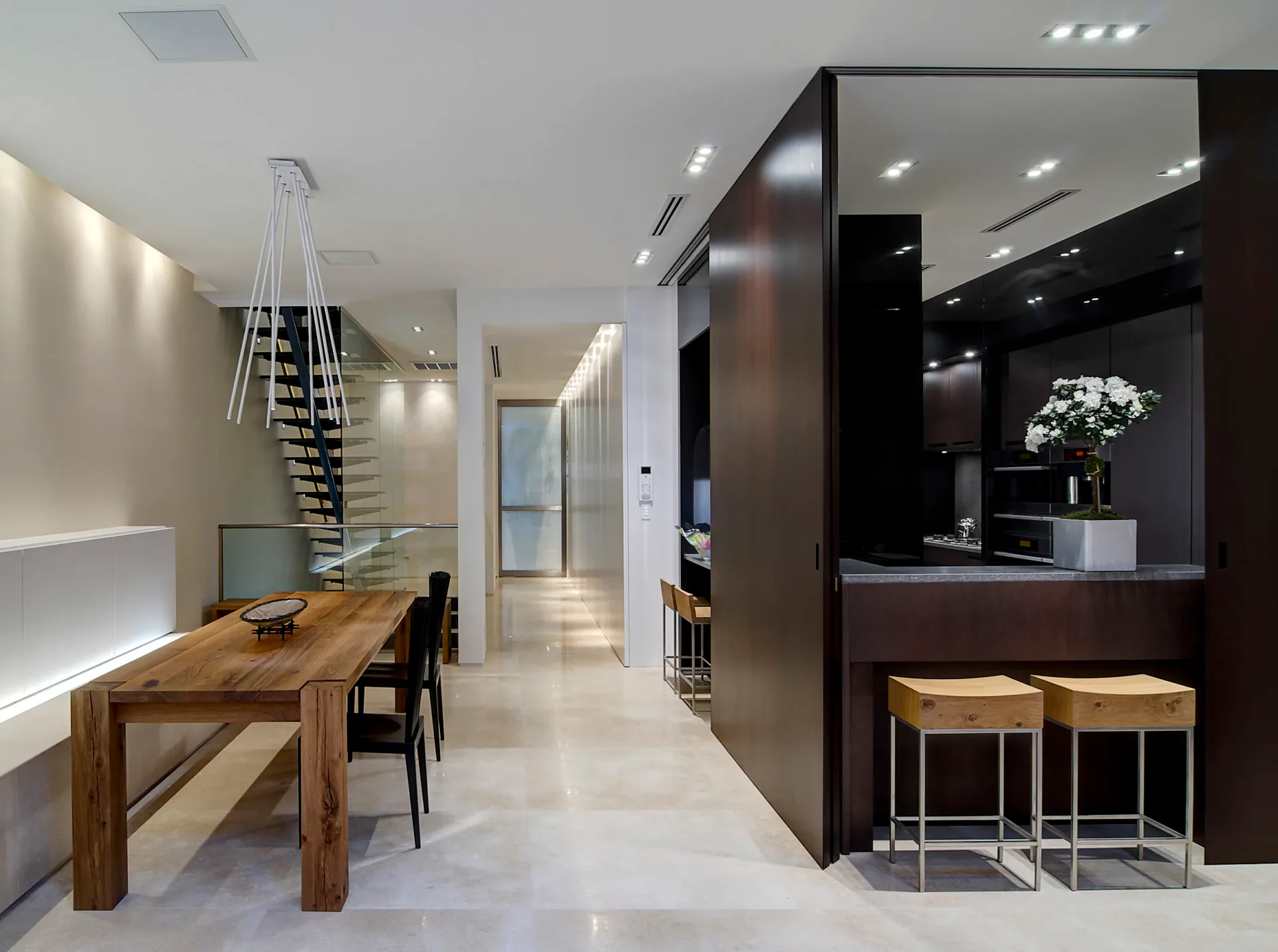 Modern kitchen and dining space with dark cabinetry, wooden table, spiral staircase, and polished concrete floors, designed by Leopoldo Rosati.