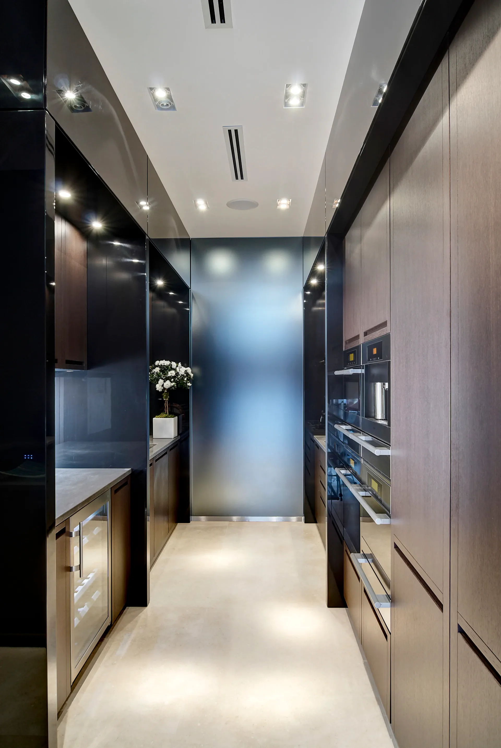 Modern galley kitchen with black cabinetry, light wood accents, frosted glass partition, recessed ceiling lights, and integrated appliances by Leopoldo Rosati.