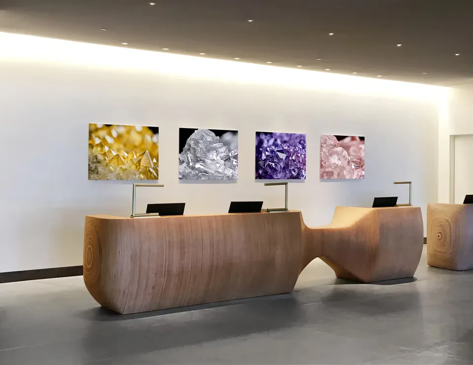 Modern reception desk with curved walnut wood design, polished concrete floor, and four colorful crystalline artworks mounted on white wall above by Leslie Ann Wigon.