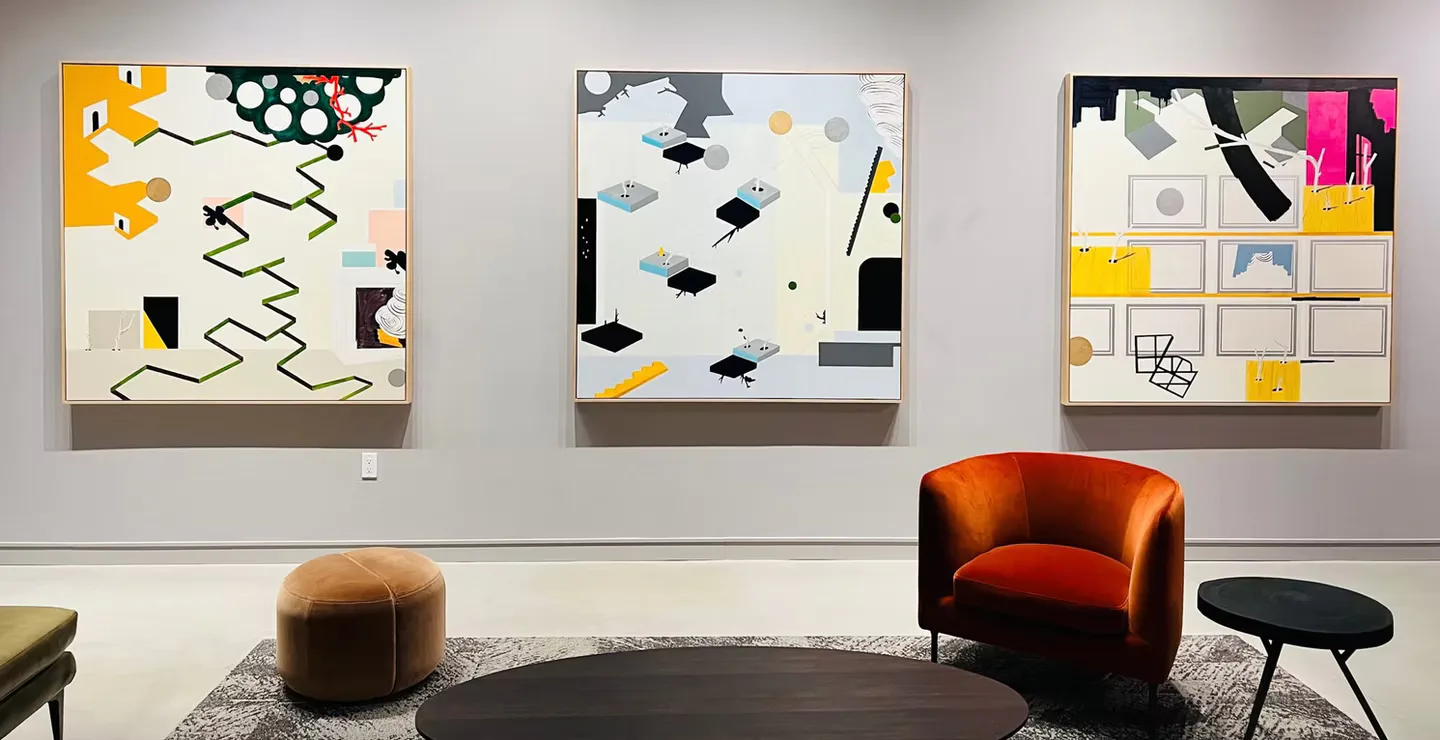 Modern interior with orange barrel chair and black ottoman facing three abstract artworks on white wall by Leslie Ann Wigon.