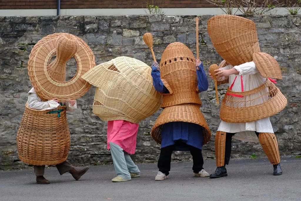 Interactive woven basket sculpture installation with figures wearing large architectural wicker forms, creating playful human-scale art piece by Lewis Prosser.