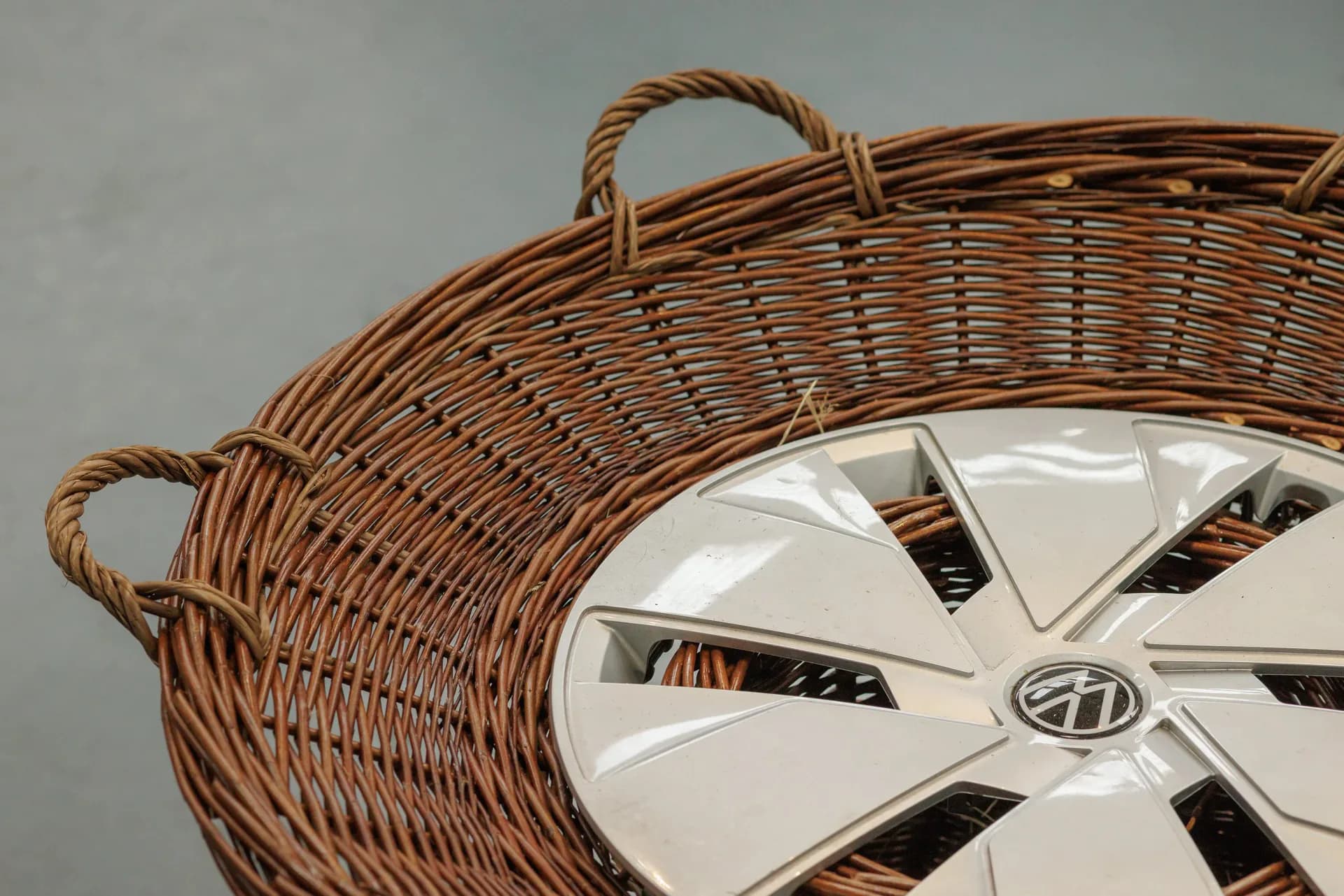Woven wicker basket with rope handles and white decorative wheel detail, showcasing craftsmanship and textural design by Lewis Prosser.