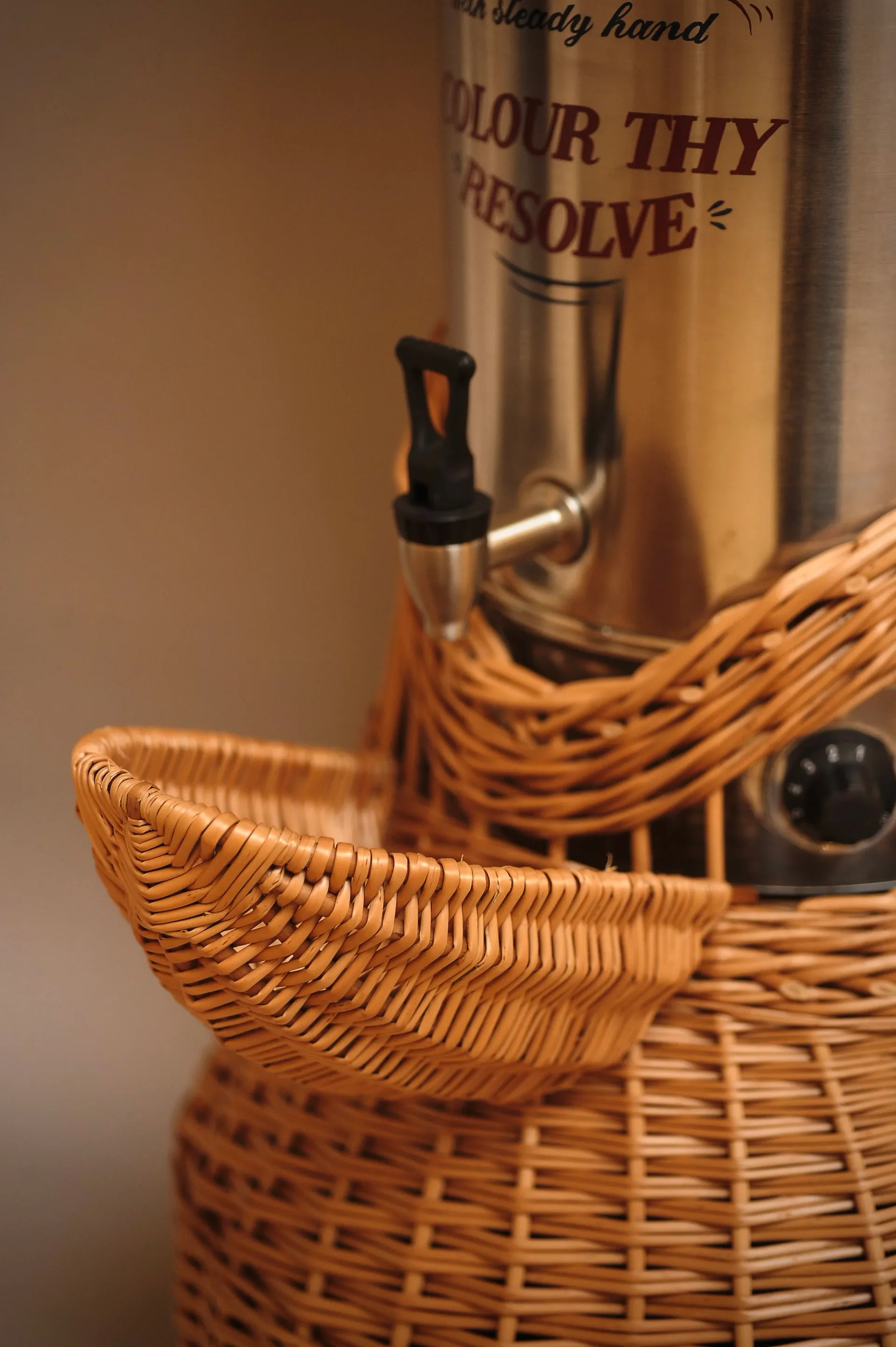 Woven wicker basket with handles holding a vintage glass bottle with black stopper and decorative label, styled product photography by Lewis Prosser.