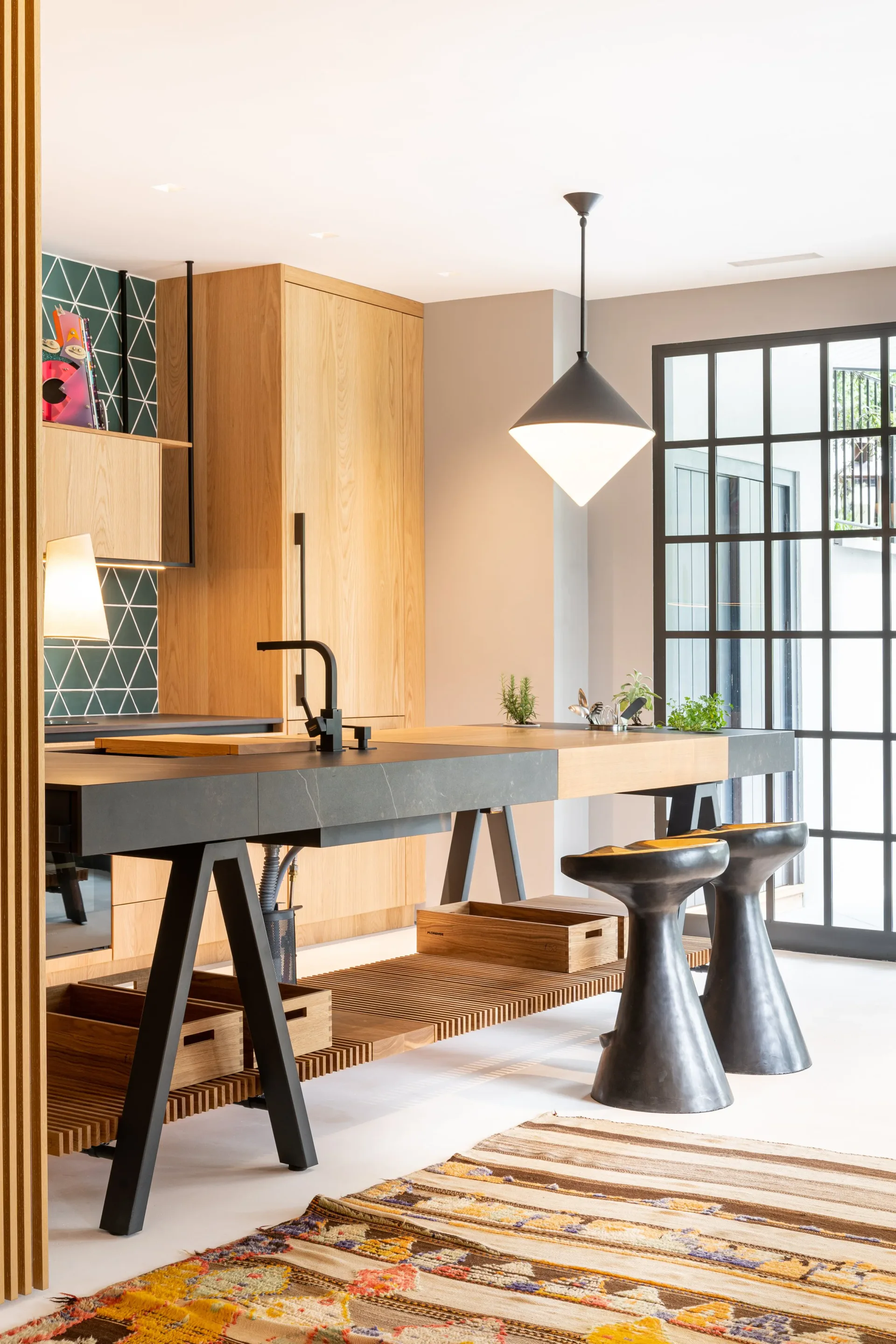 Modern kitchen workspace with natural wood cabinetry, black metal pendant light, geometric tile backsplash, and geometric patterned rug by Leyden Lewis.