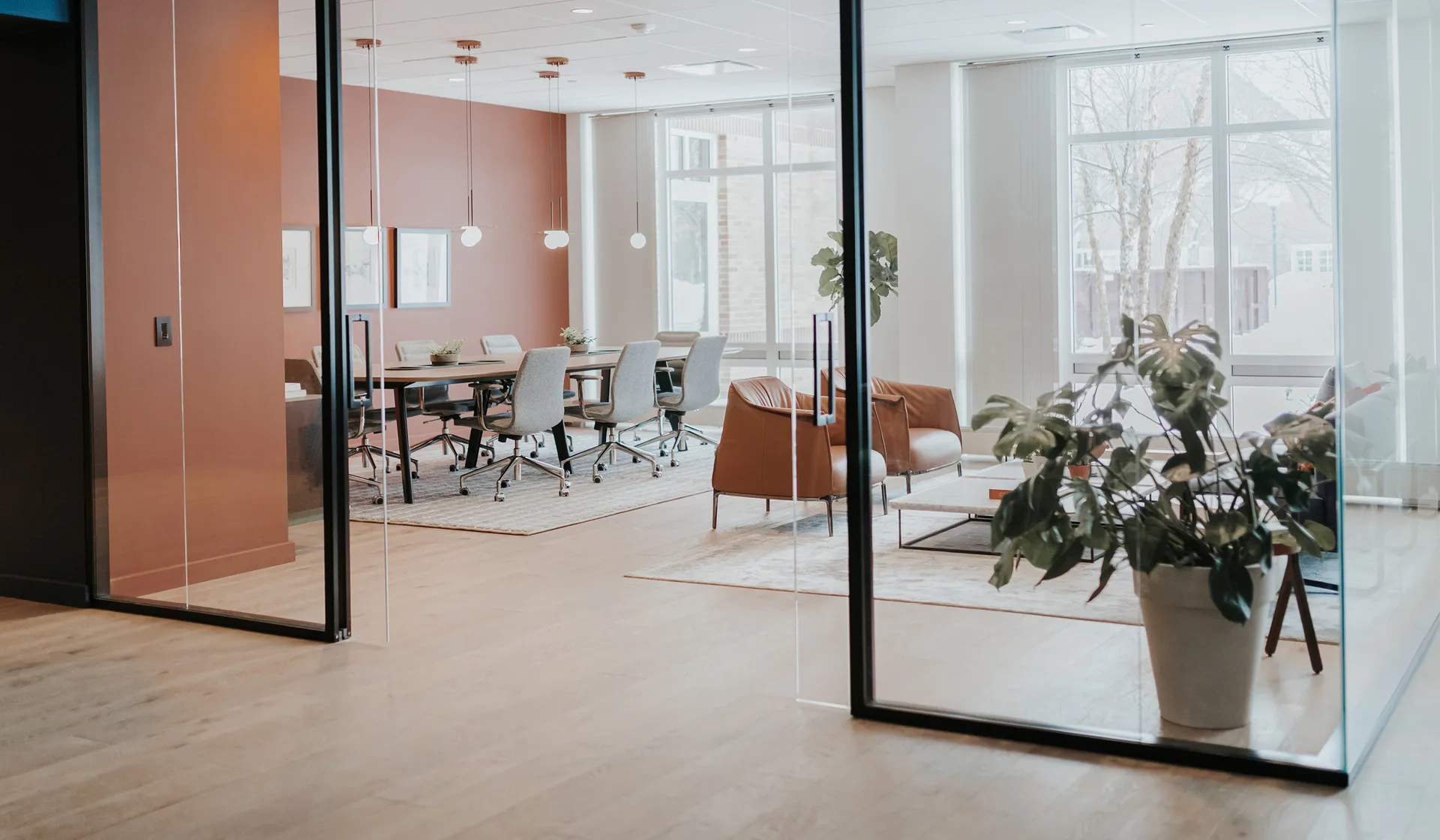 Modern office interior with glass partitions, terracotta accent wall, wooden flooring, and contemporary furniture arranged in open-plan layout by Liam Han.