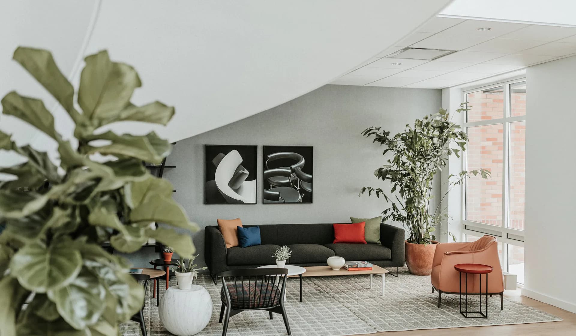Modern loft interior with black sofa, cognac leather chair, and abundant natural light; designed by Liam Han.