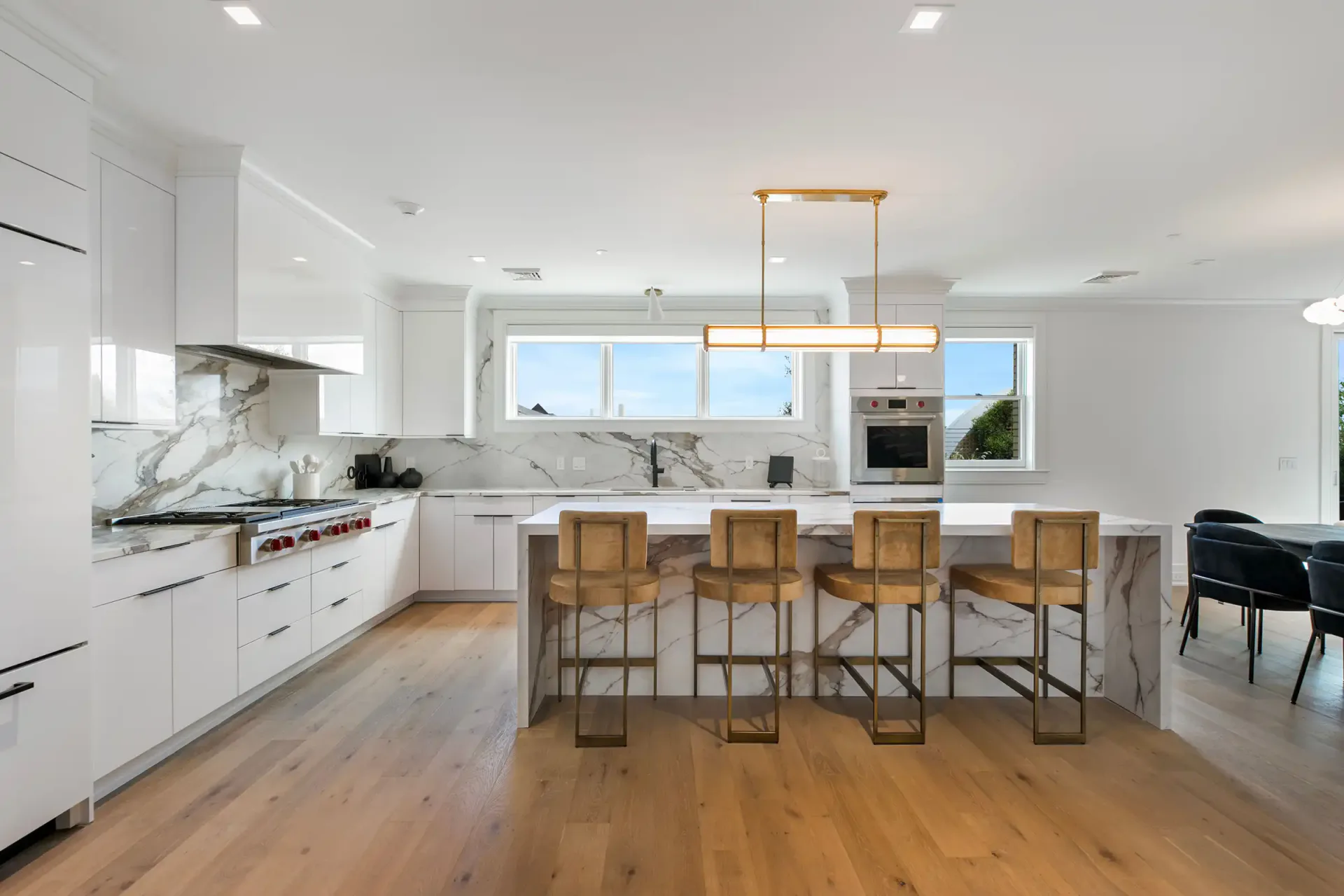 Modern white kitchen with marble backsplash and wooden island featuring rattan bar stools, designed by Lindsay Fauth.