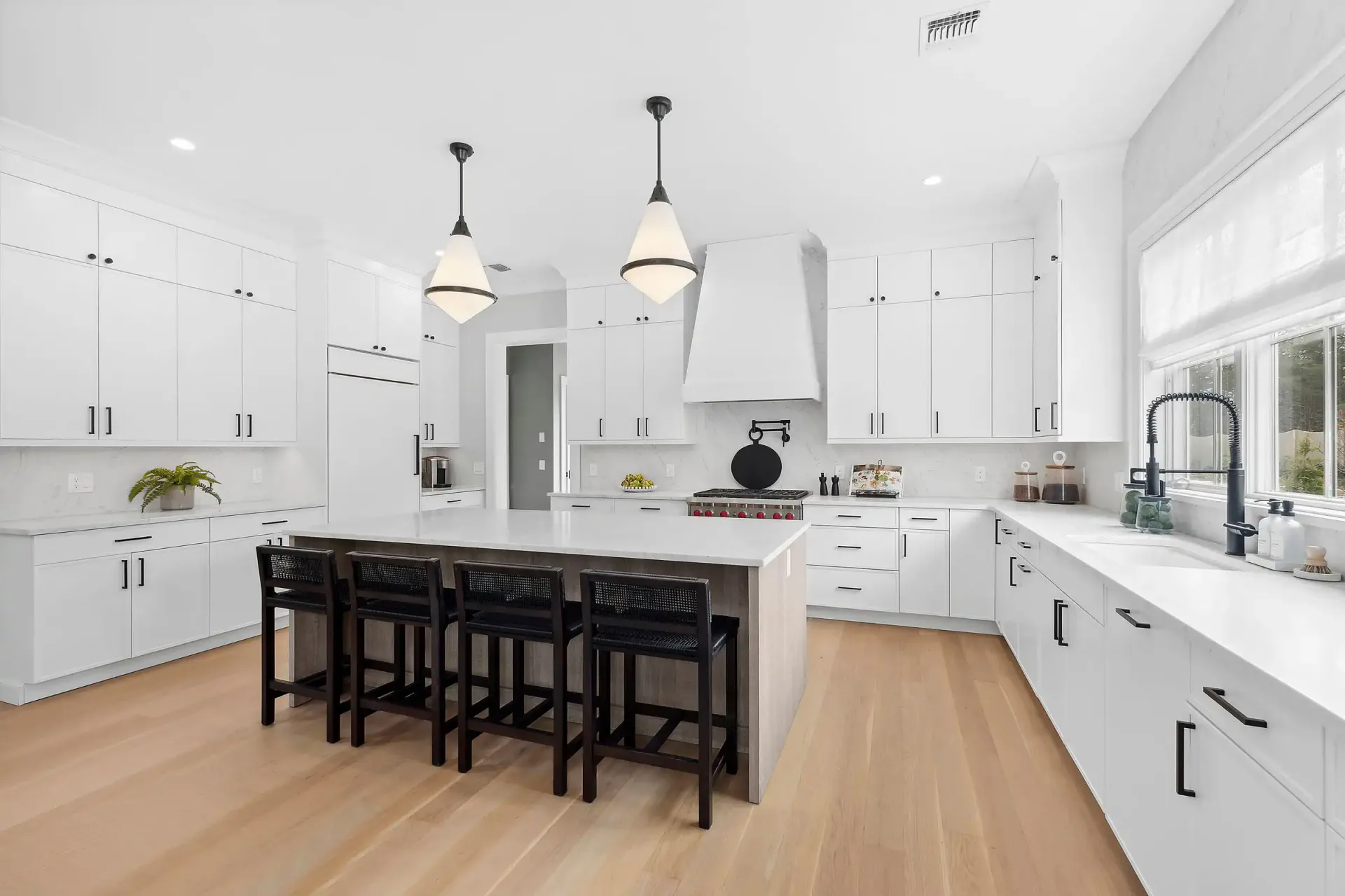 Modern white kitchen with black island and stools, pendant lighting, and light wood flooring by Lindsay Fauth.