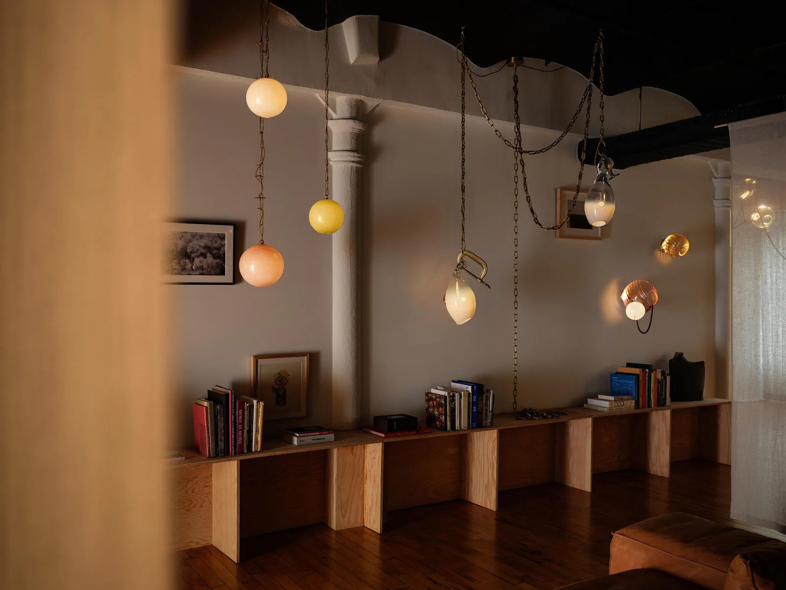 Warm wooden retail or gallery space with suspended globe pendant lights in amber and cream tones, minimalist wooden display blocks, and industrial ceiling details by Lindsey Adelman.