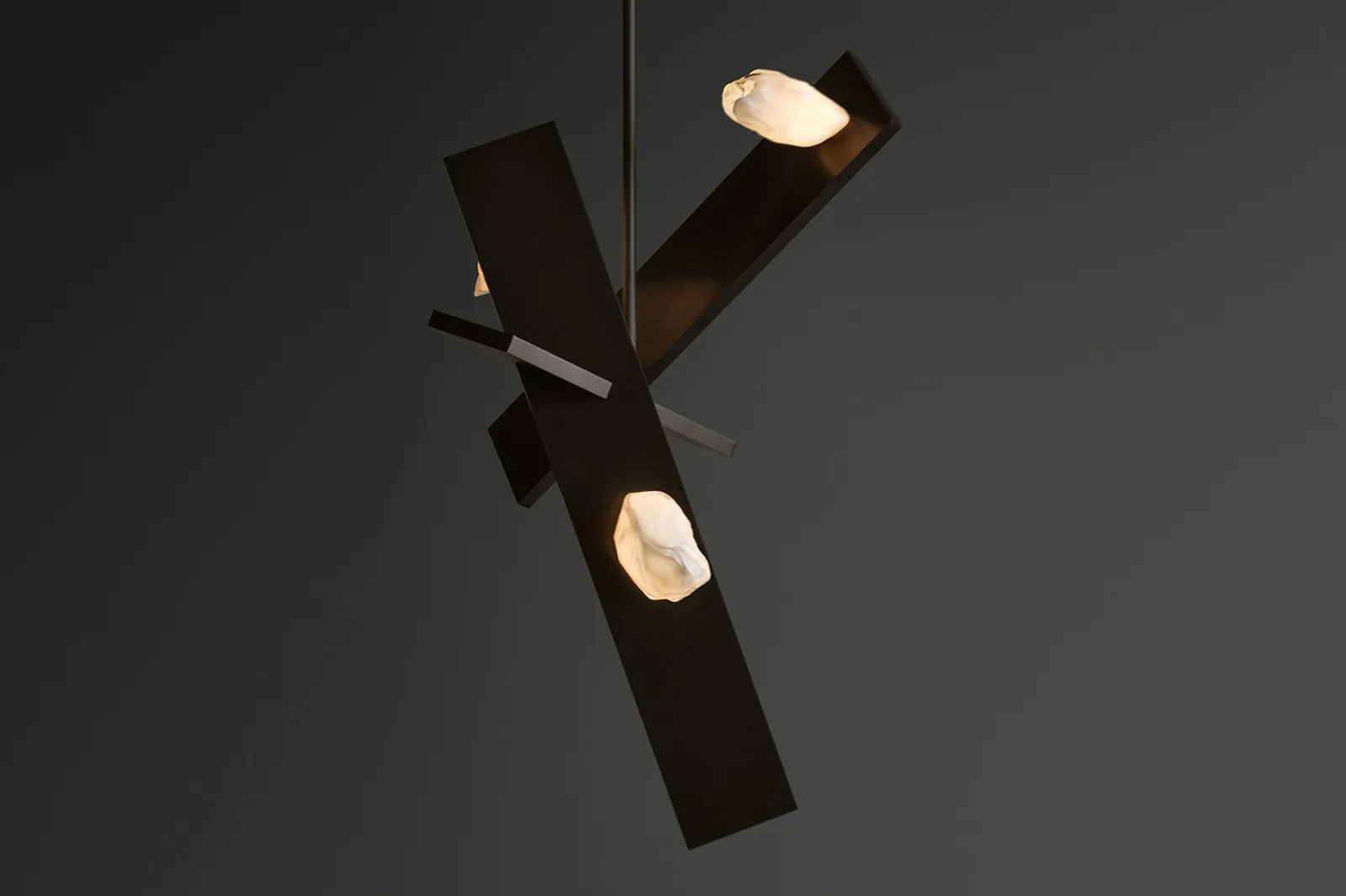 Abstract lighting installation with dark geometric cylinders and glowing cream-colored circular elements arranged in a sculptural composition by Lindsey Adelman.