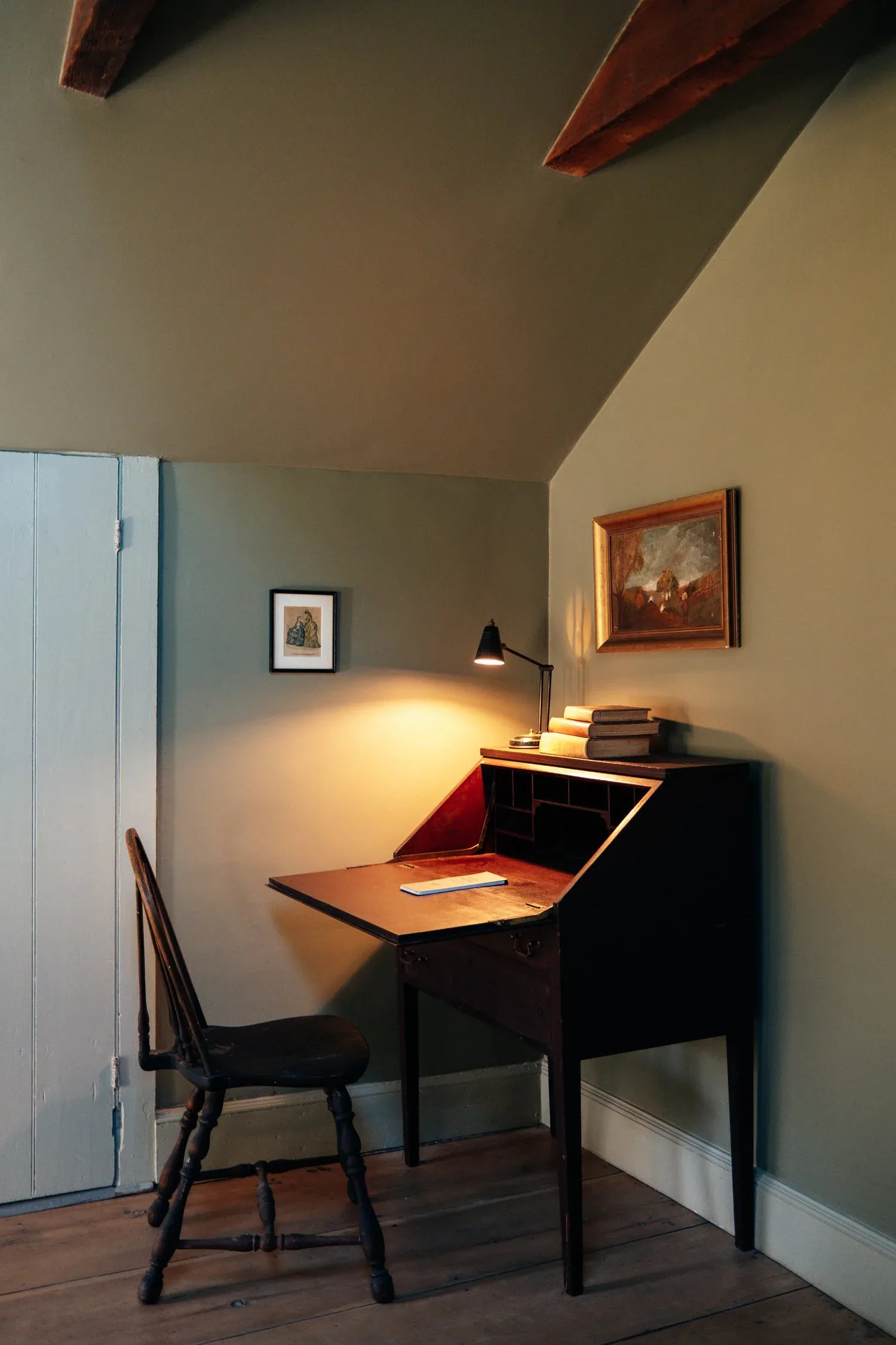 A minimalist home office nook featuring a black desk with wooden top, black chair, and warm pendant lighting against cream walls, designed by Linnea Zeiloth.