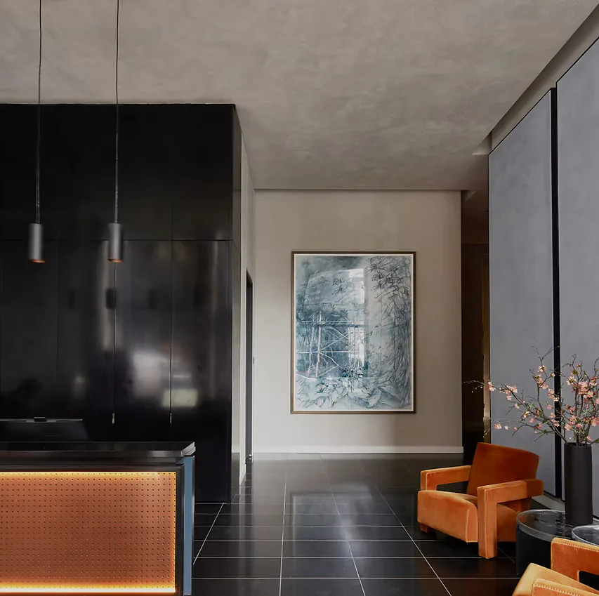 Modern interior with black cabinetry, orange accent chair, pendant lights, and blue-toned artwork by Liong The.