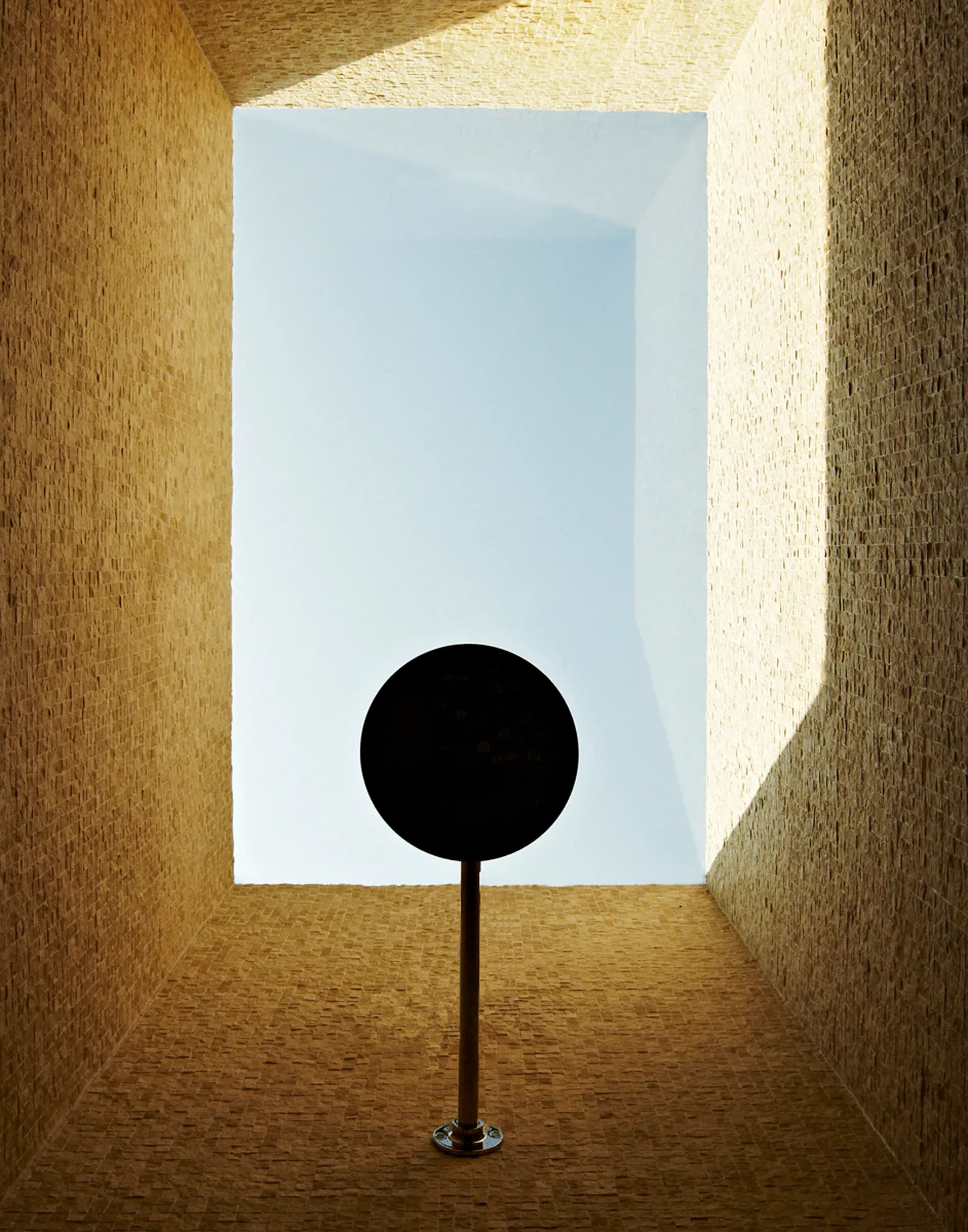 Minimalist architectural rendering of a concrete corridor with a black spherical form centered in front of a bright blue sky opening, by Lisa Dang.
