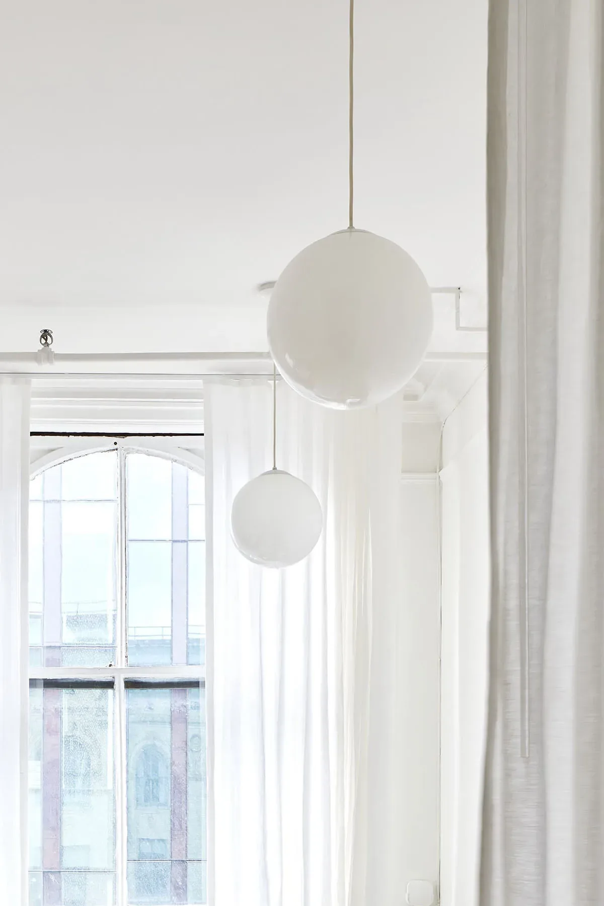 Minimalist interior with two hanging spherical white pendant lights suspended from ceiling in bright, naturally-lit space by Lisa Galano.