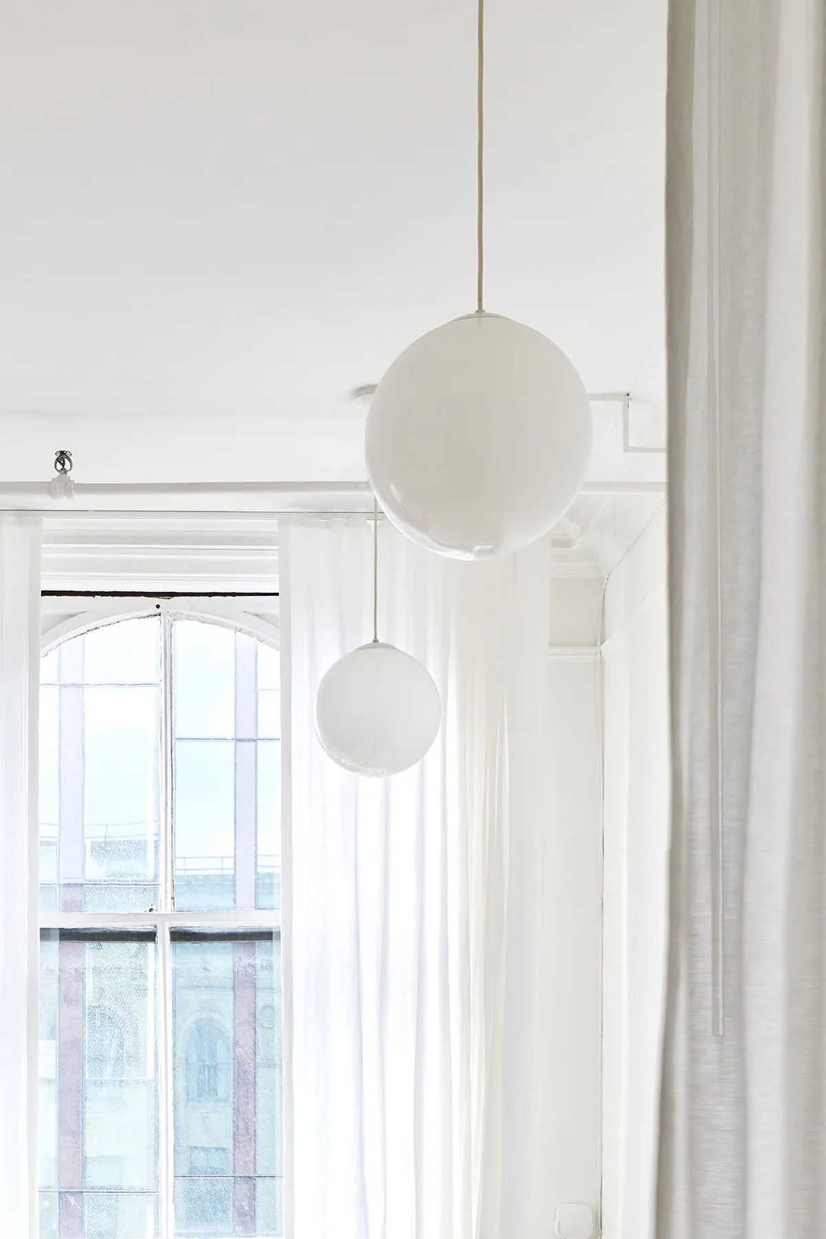 Minimalist interior with two hanging spherical pendant lights in soft white, bright natural light from tall windows, and clean modernist aesthetic by Lisa Galano.