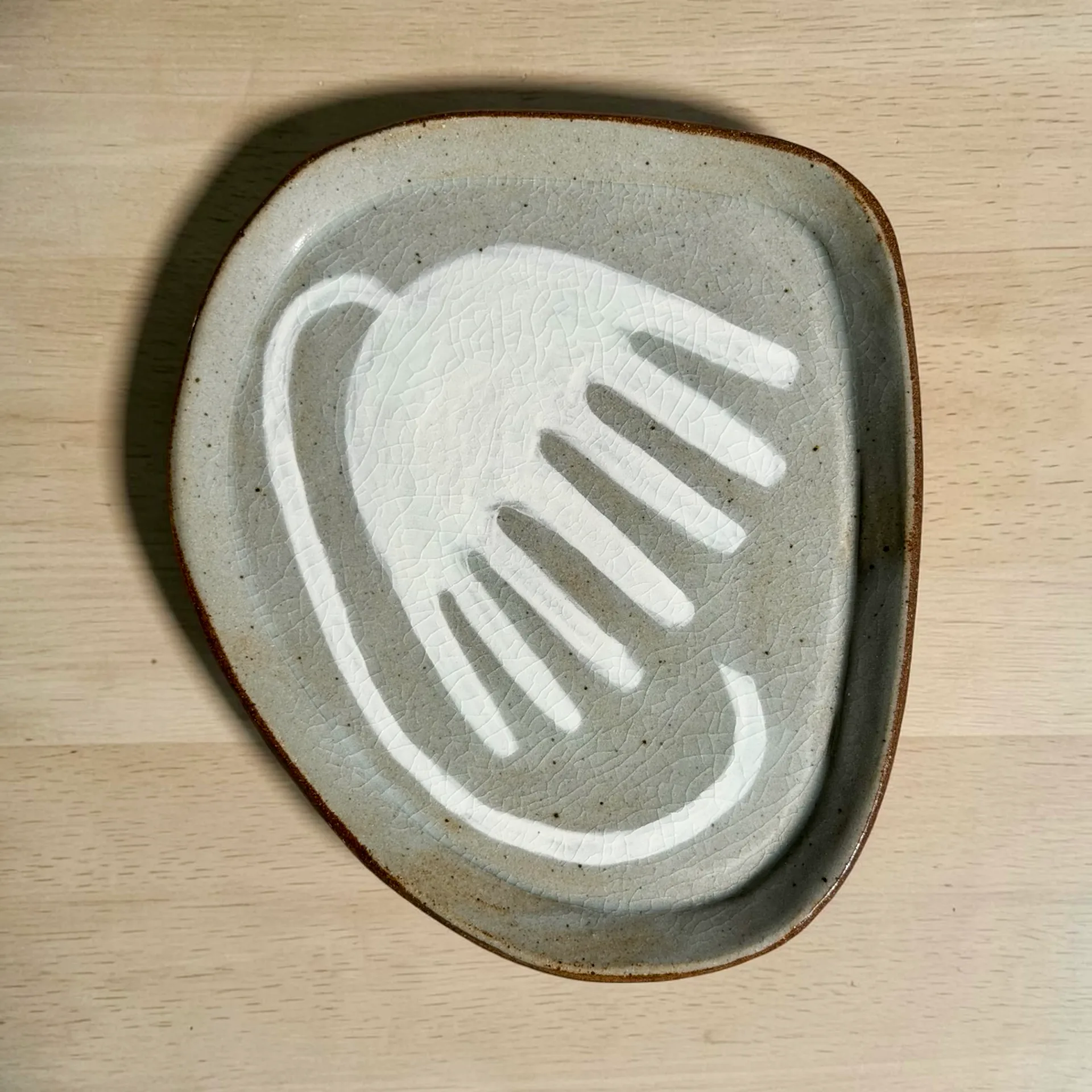 Concrete ceramic dish with white-painted hand and comb motif, minimalist design by Lisa Jakobsberg.