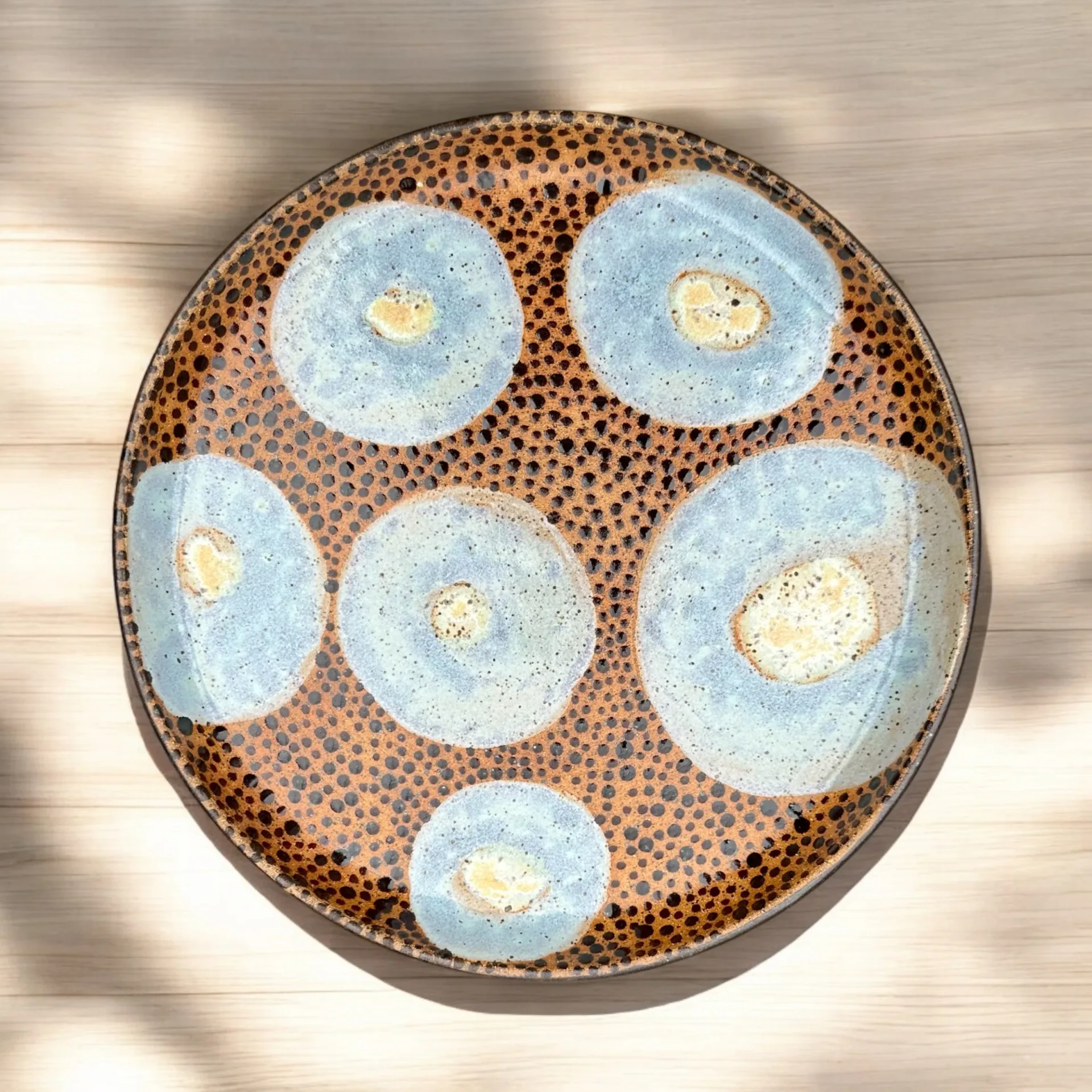Ceramic serving platter with terracotta speckled glaze featuring six blue dishes with cream-colored centers, arranged in circular composition by Lisa Jakobsberg.