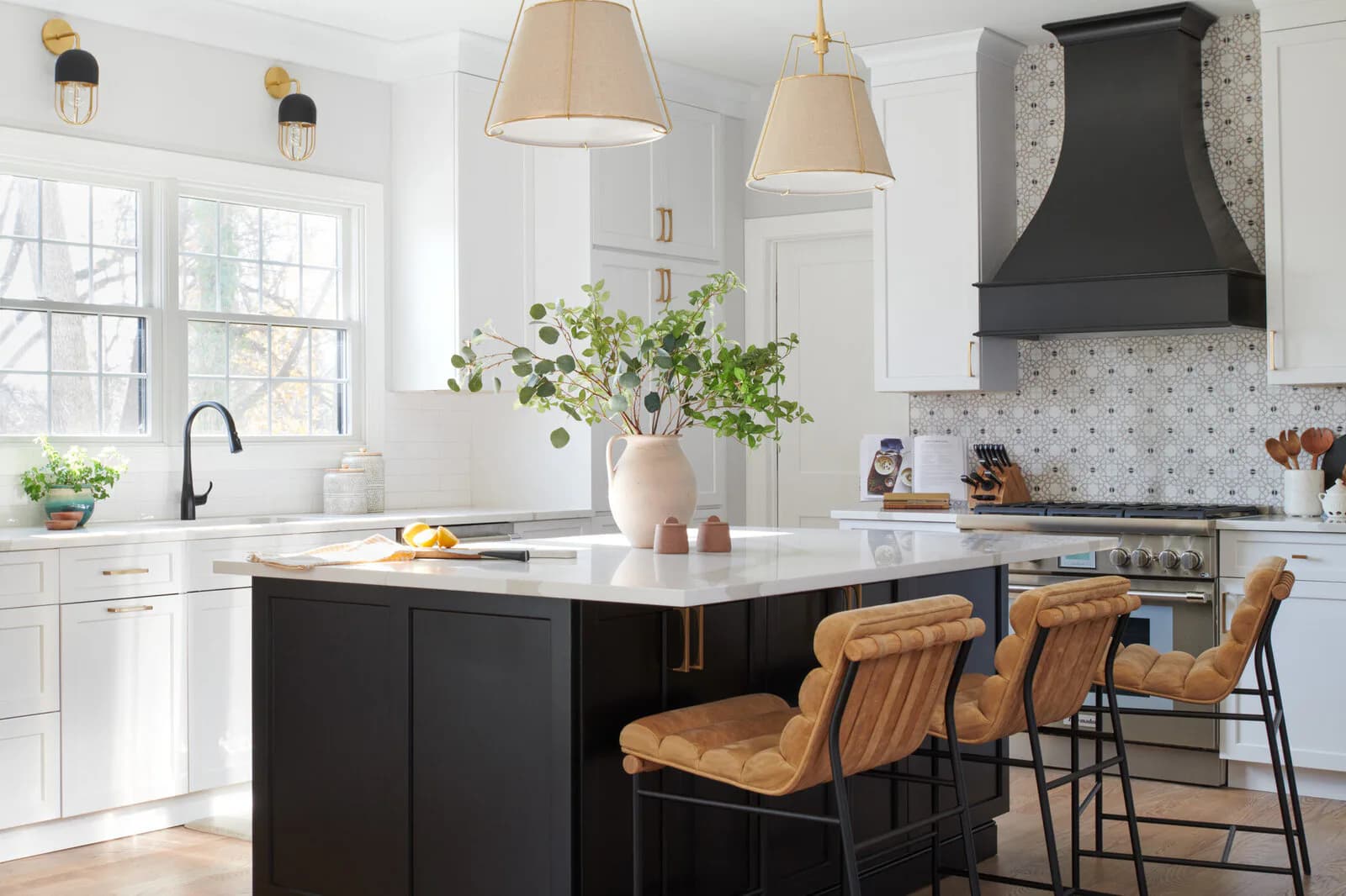 Modern kitchen with white cabinetry, black island, marble countertops, and warm wood bar seating by Lisa Spicer.