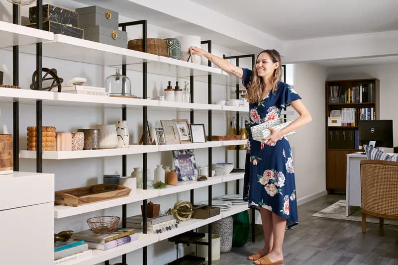 Modern shelving unit with white shelves and black metal frame displaying curated home goods and books in a bright residential interior by Lisa Spicer.