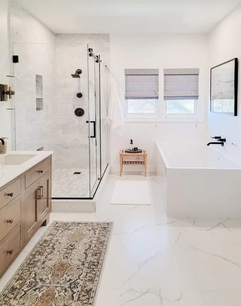 Modern primary bathroom with marble flooring, white subway tile shower, natural wood vanity, and freestanding soakable bathtub by Lisa Spicer.