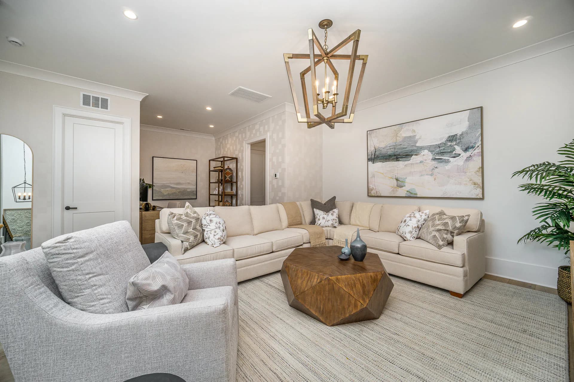 Bright, neutral living room with cream upholstered seating, wood accent table, pendant lighting, and coastal artwork by Liz Aragona.