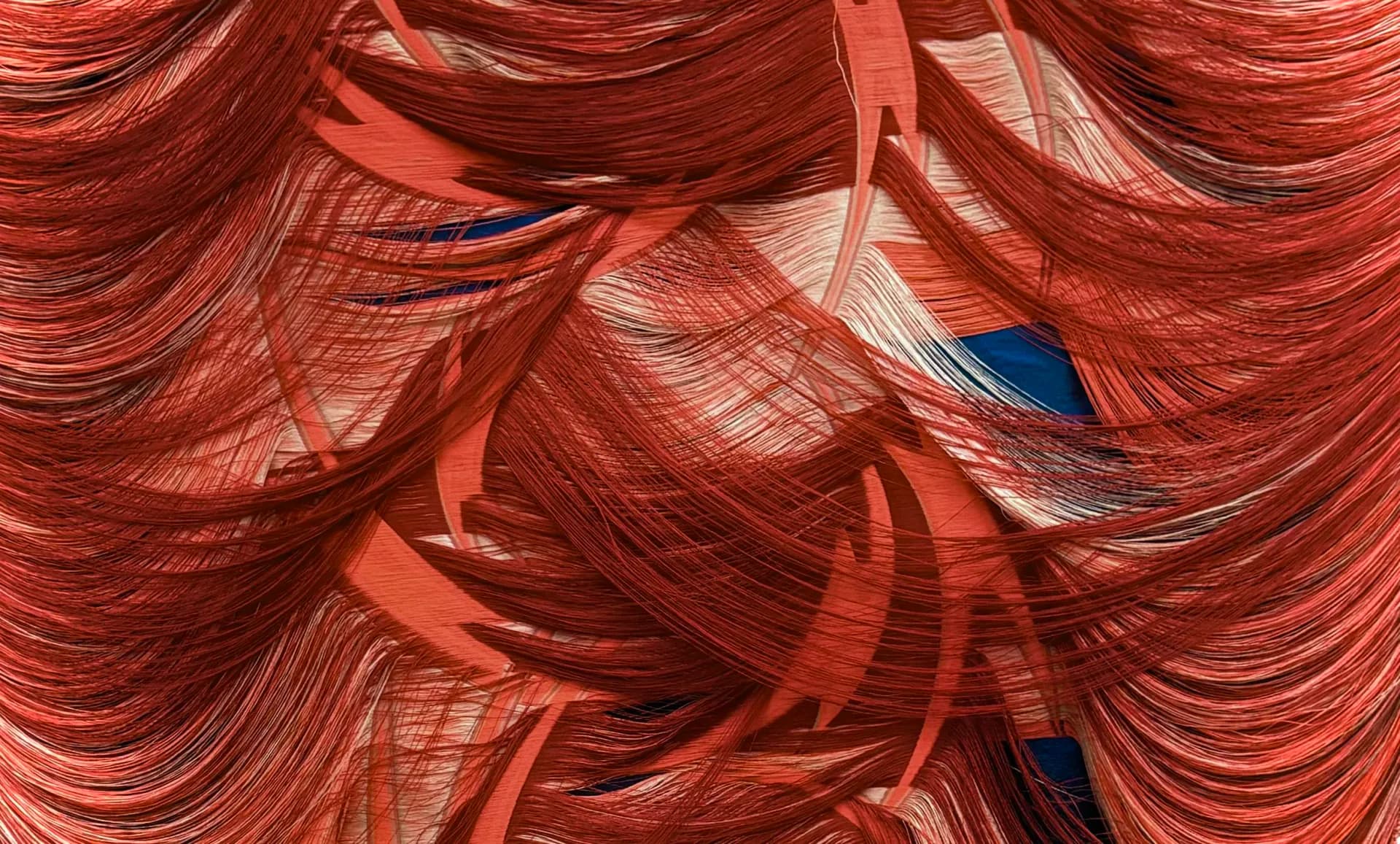 Flowing red fabric installation with dramatic layered drapery and a small blue accent element, creating an undulating textile composition by Liz Collins.