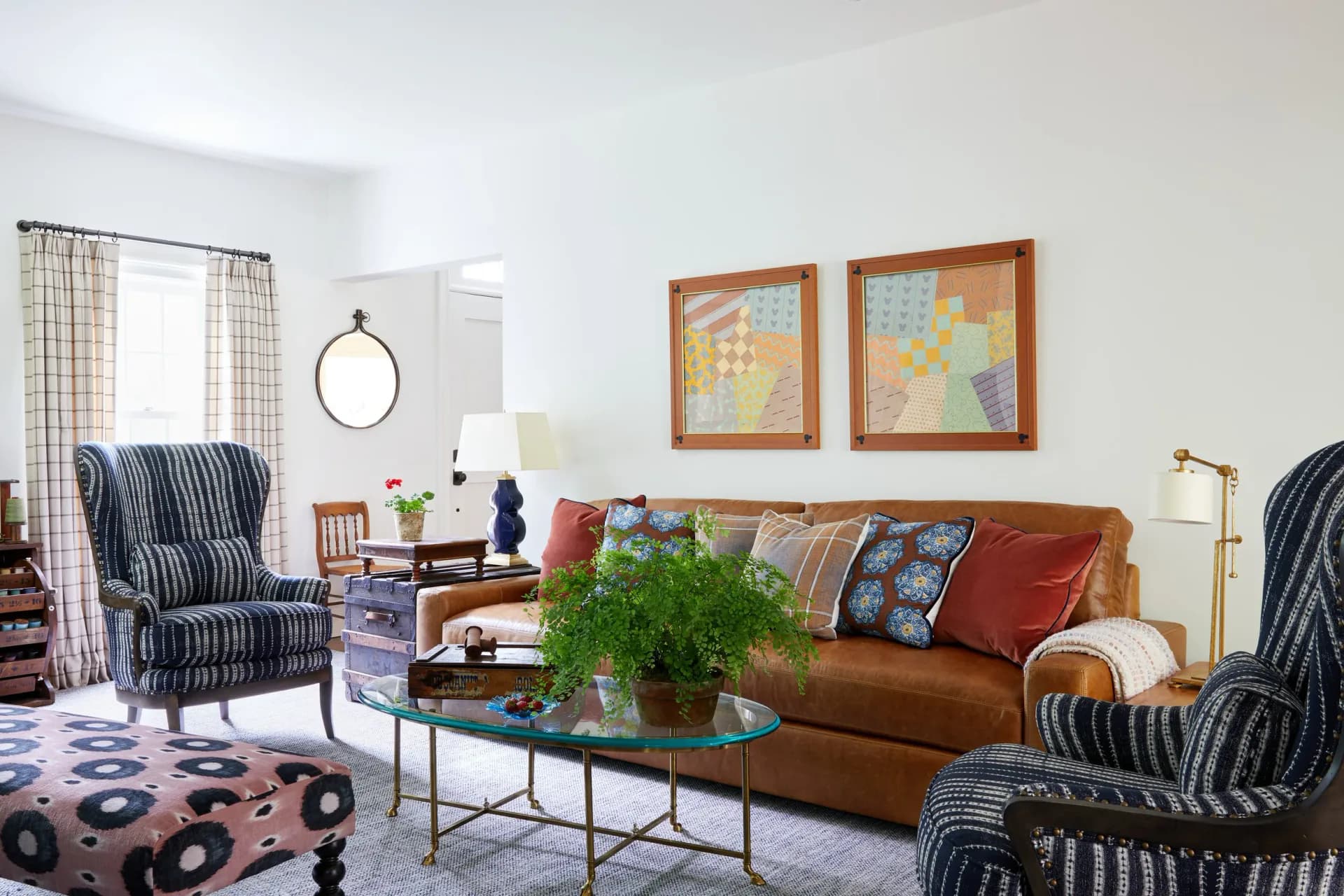 A bright living room features a rust-colored sofa, striped armchairs, patterned rug, wooden side tables, and botanical elements, designed by Liza Kuhn.