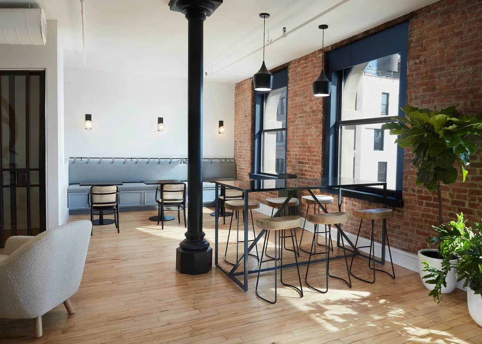 Modern loft interior with exposed brick walls, wooden flooring, black structural column, bar seating, and contemporary furniture by Lizi Gegenava.
