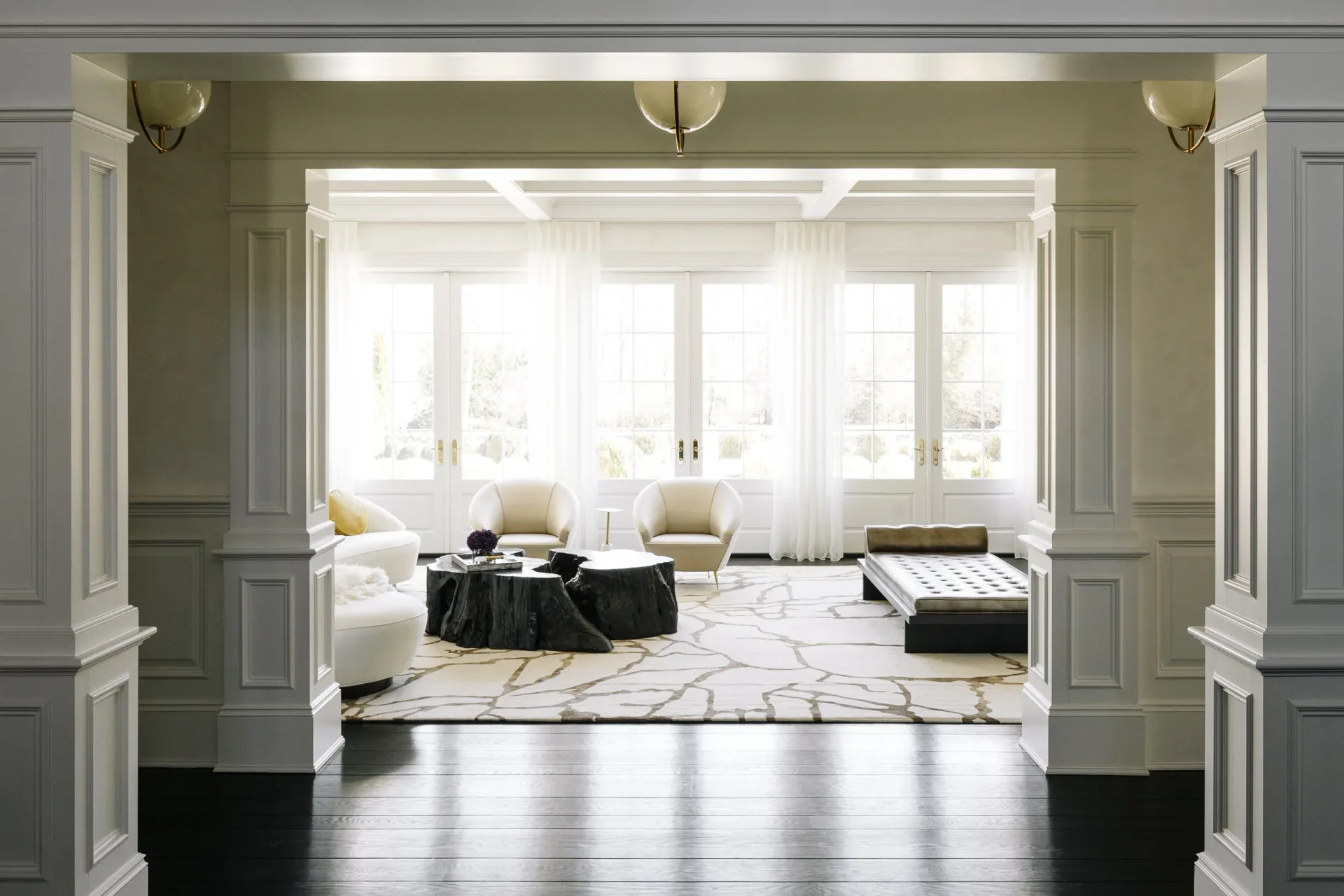 Elegant sunlit sitting room with pale green walls, white trim, brass sconces, marble flooring, and contemporary furnishings, designed by Lori Margolis.