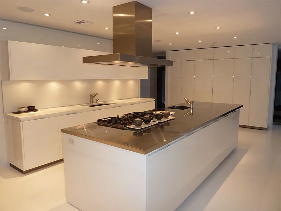 Modern white kitchen with waterfall-edge island, gas cooktop, bronze hood, and minimalist cabinetry by Lorraine Frye.