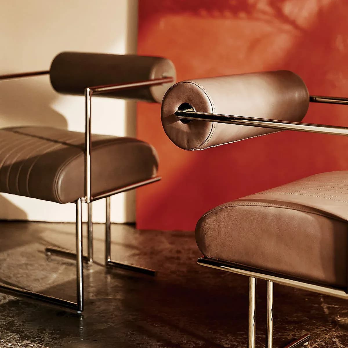 Modern lounge interior featuring sculptural brown leather chairs with curved metal frames against warm terracotta walls by Luam Melake.