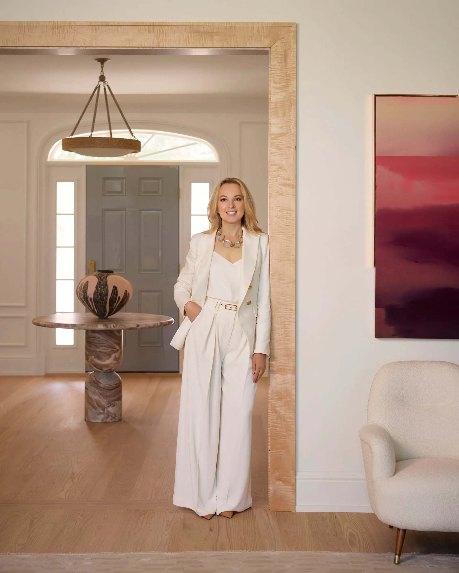 Modern entryway with warm wood flooring, minimalist white palette, sculptural pedestal side table, and contemporary artwork on wall by Luba Libarikian.