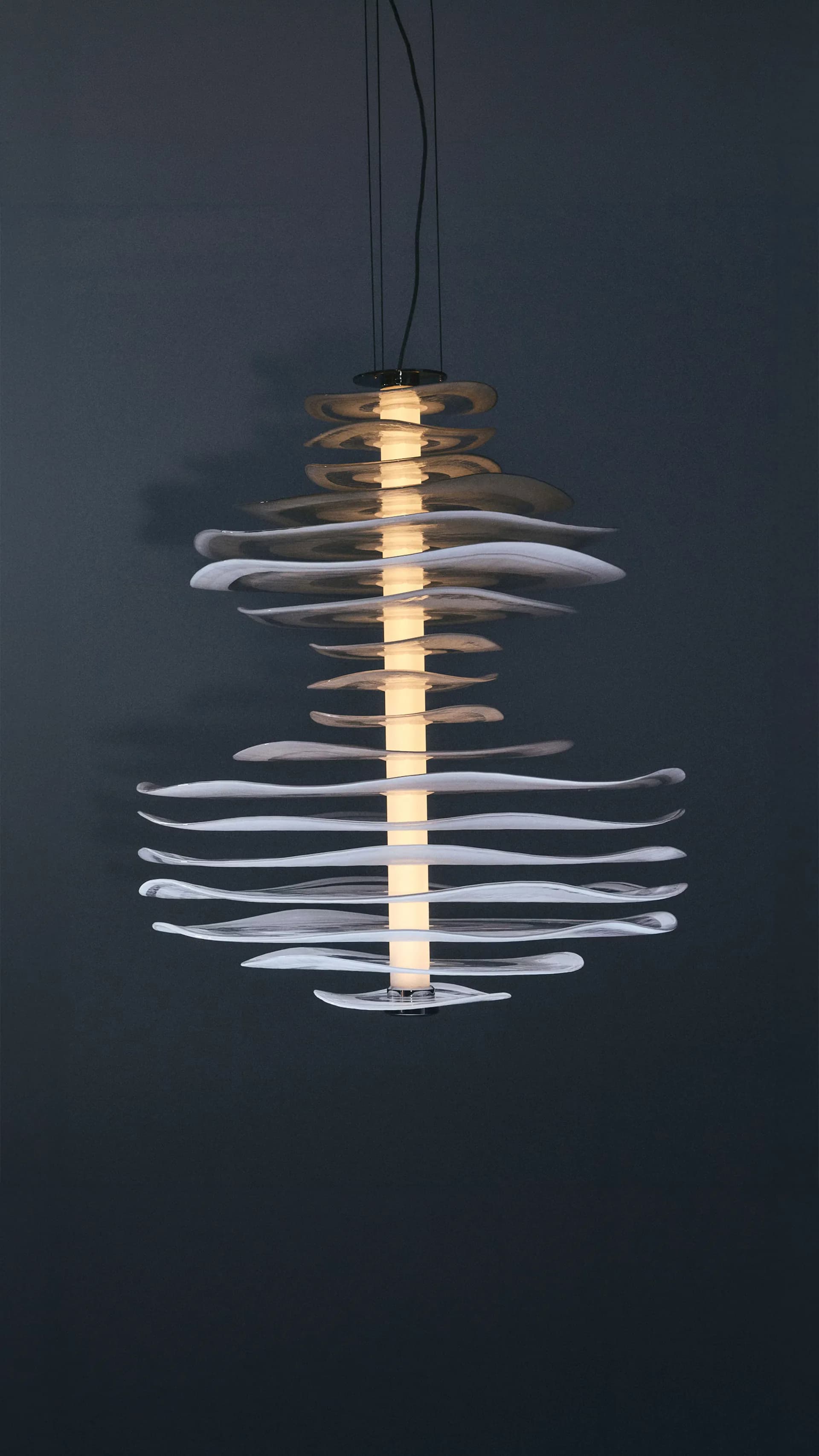 Pendant lighting fixture with stacked curved elements in bronze and white tones arranged around a central illuminated core, by Luca Nichetto.