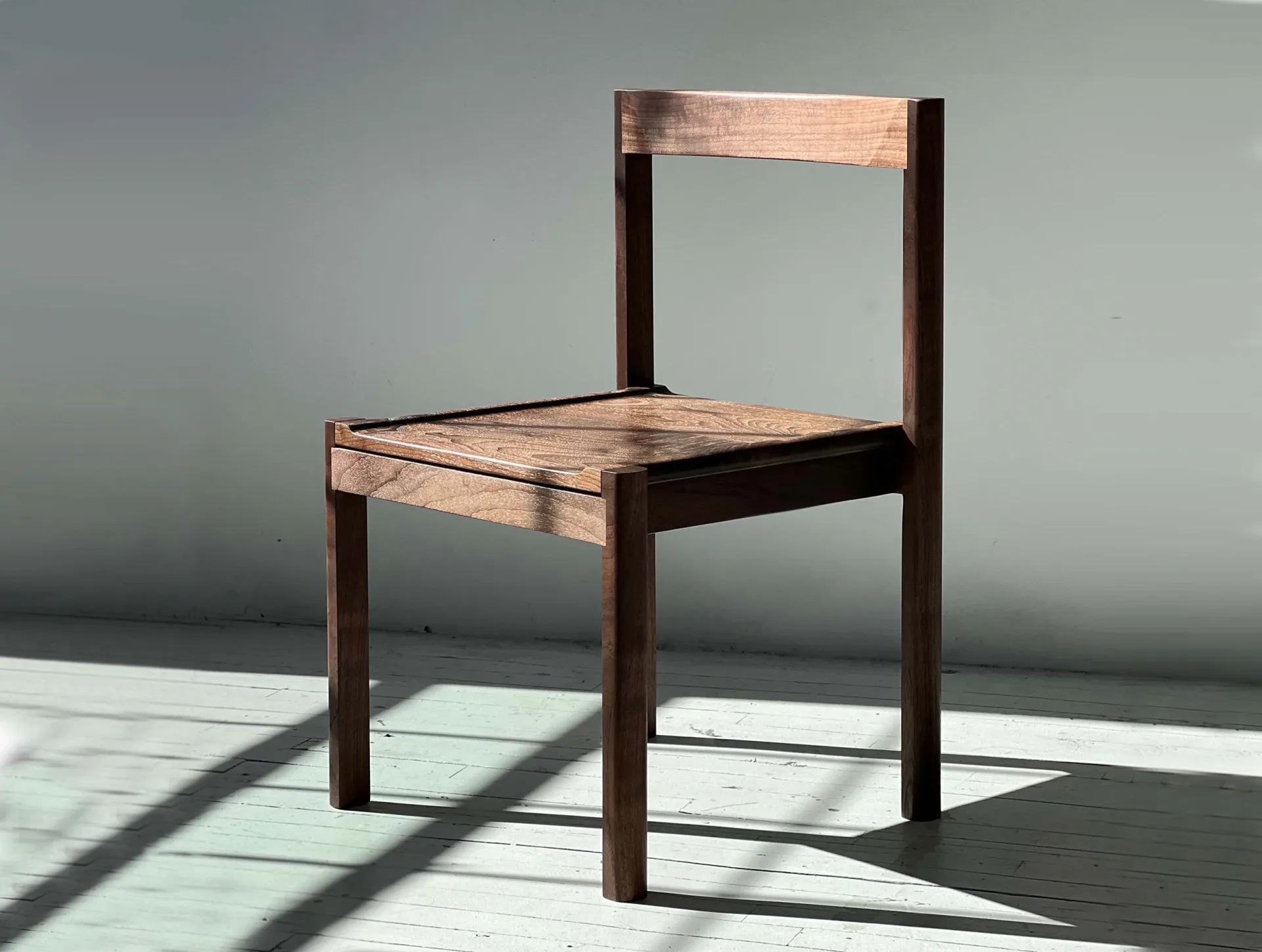 Minimalist wooden chair with dark brown frame and light wood seat and backrest, rendered with precise lighting and shadows by Luke Fasano.