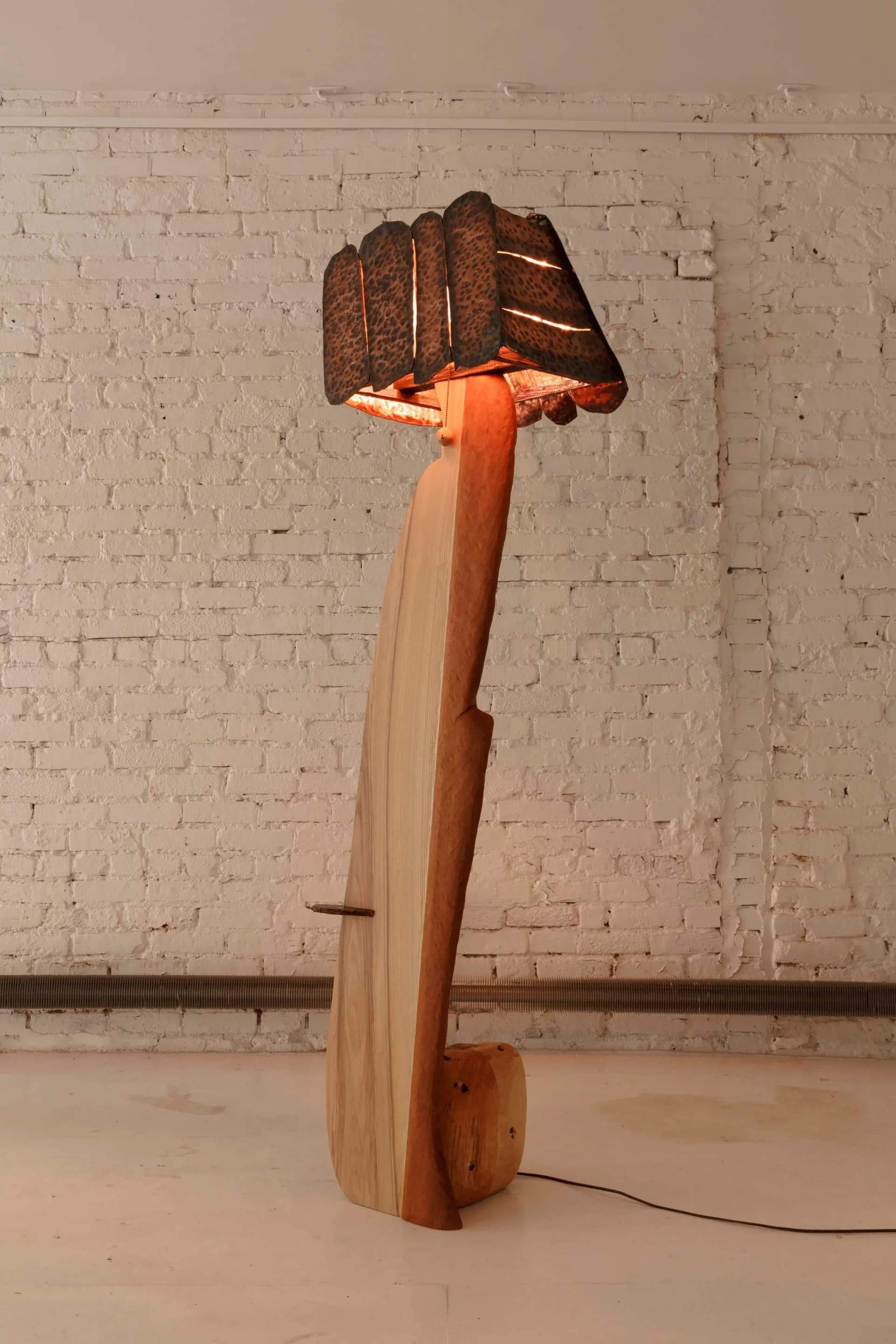 Wooden sculptural lighting installation featuring a large clenched fist form atop a tapered wooden base with orange accent, by Luke Malaney.