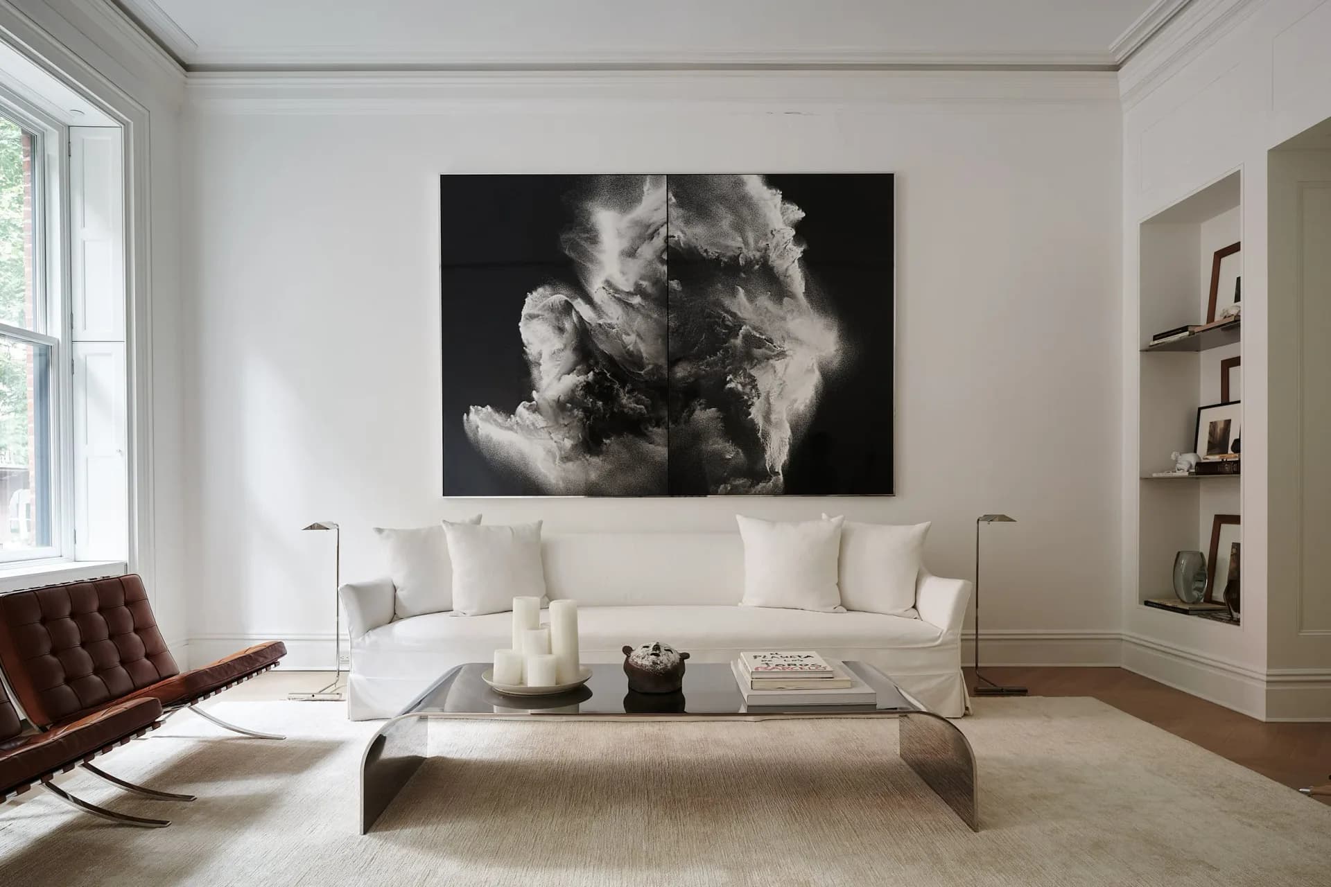 Minimalist living room with cream sofa, burgundy leather chair, floating table, and abstract black-and-white artwork above, designed by Khanh Luu.