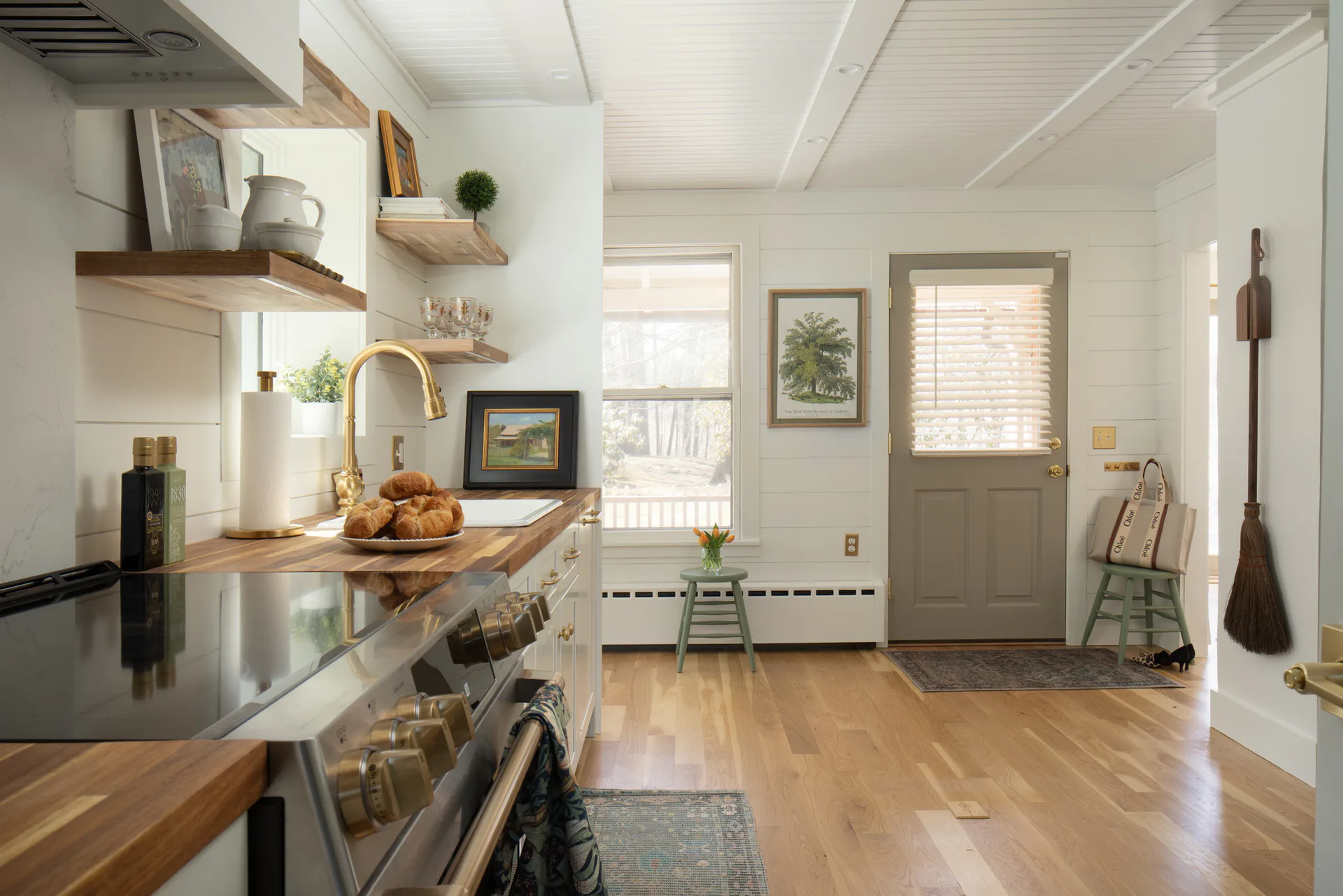 Bright farmhouse kitchen with wood countertops, black stove, open shelving, and view to mudroom entry, designed by MacHayla Karcheski.