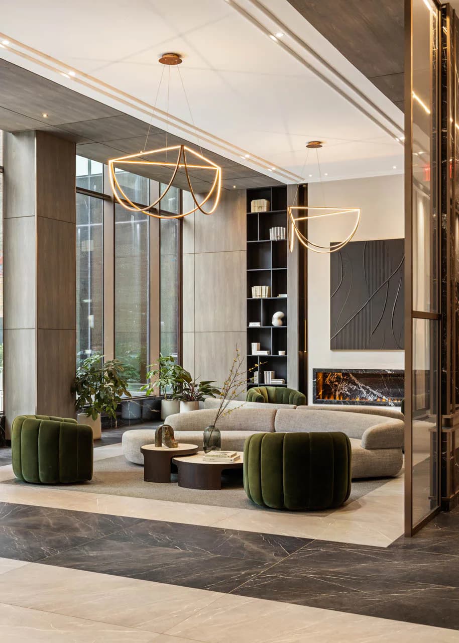 Luxury modern living room with curved cream sofa, green velvet poufs, gold pendant lighting, marble fireplace, floor-to-ceiling windows, and built-in shelving by MacKenzie Reid.