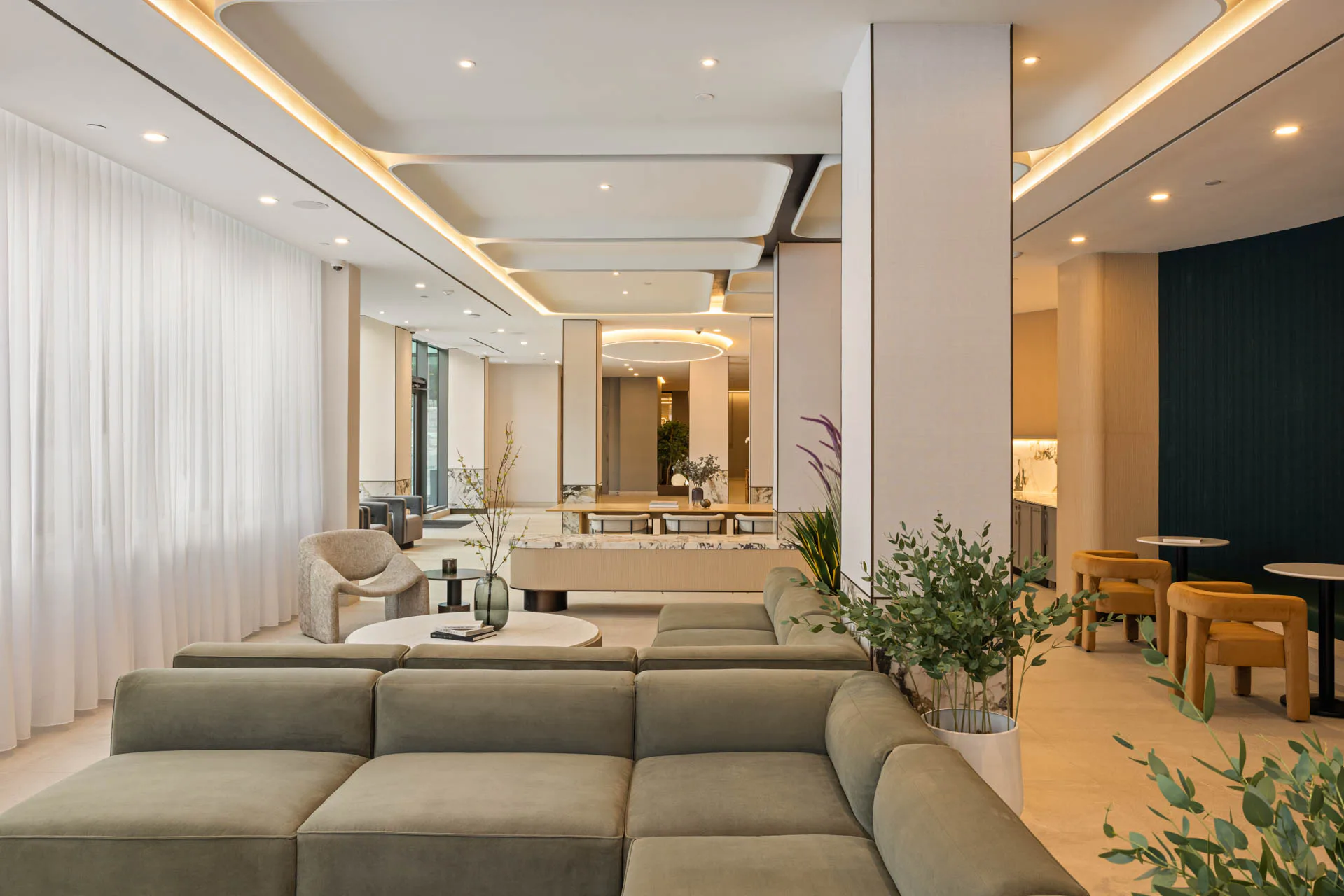 Modern living room with curved sectional sofa, warm wood flooring, and sophisticated lighting design by MacKenzie Reid.
