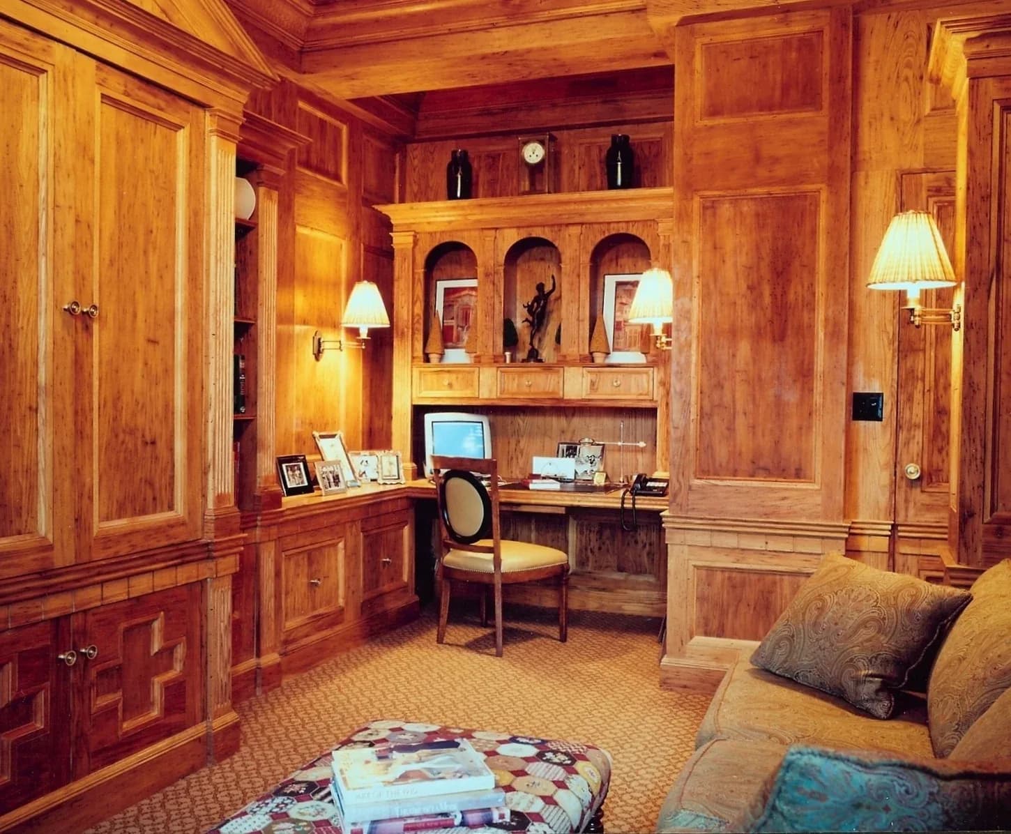 Warm wood-paneled home office with built-in cabinetry, desk, arched shelving, and upholstered seating by Marc Donnenfeld.