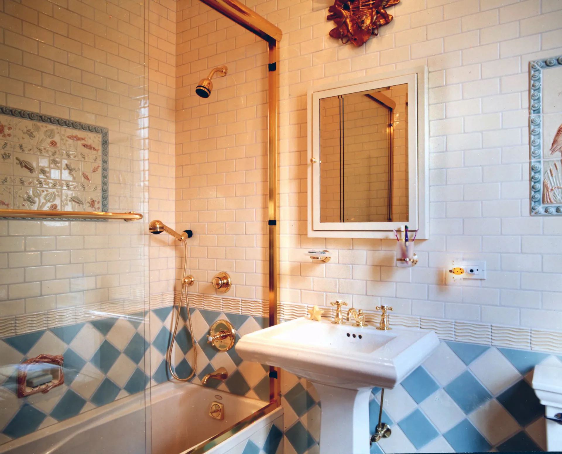 Elegant bathroom with blue and white diamond-patterned tile wainscoting, white subway tile walls, brass fixtures, and a frameless glass shower enclosure by Marc Donnenfeld.
