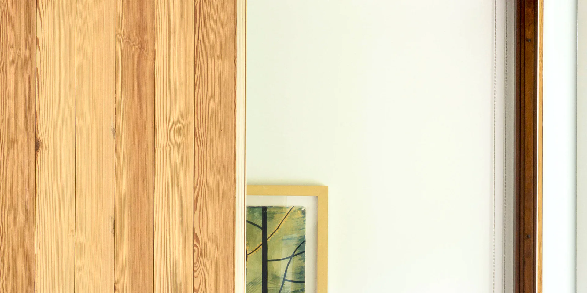 Minimalist interior detail showing natural wood paneling beside cream wall with small framed botanical artwork by Marc Leff.
