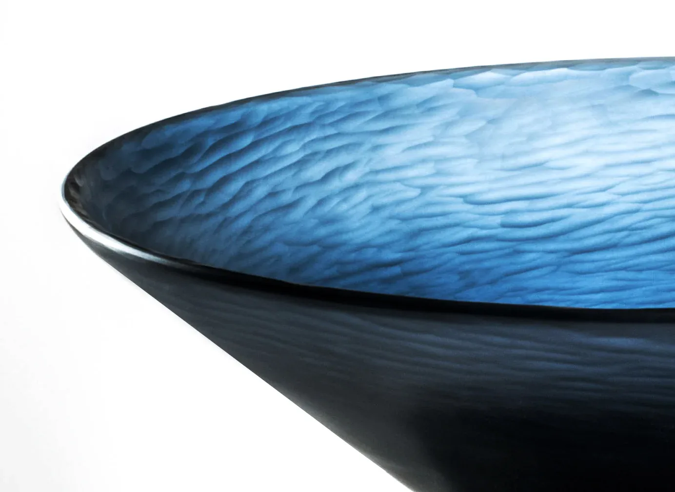 Blue and black sculptural bowl with flowing wave-textured surface and polished rim detail, minimalist product design by Marc Thorpe.