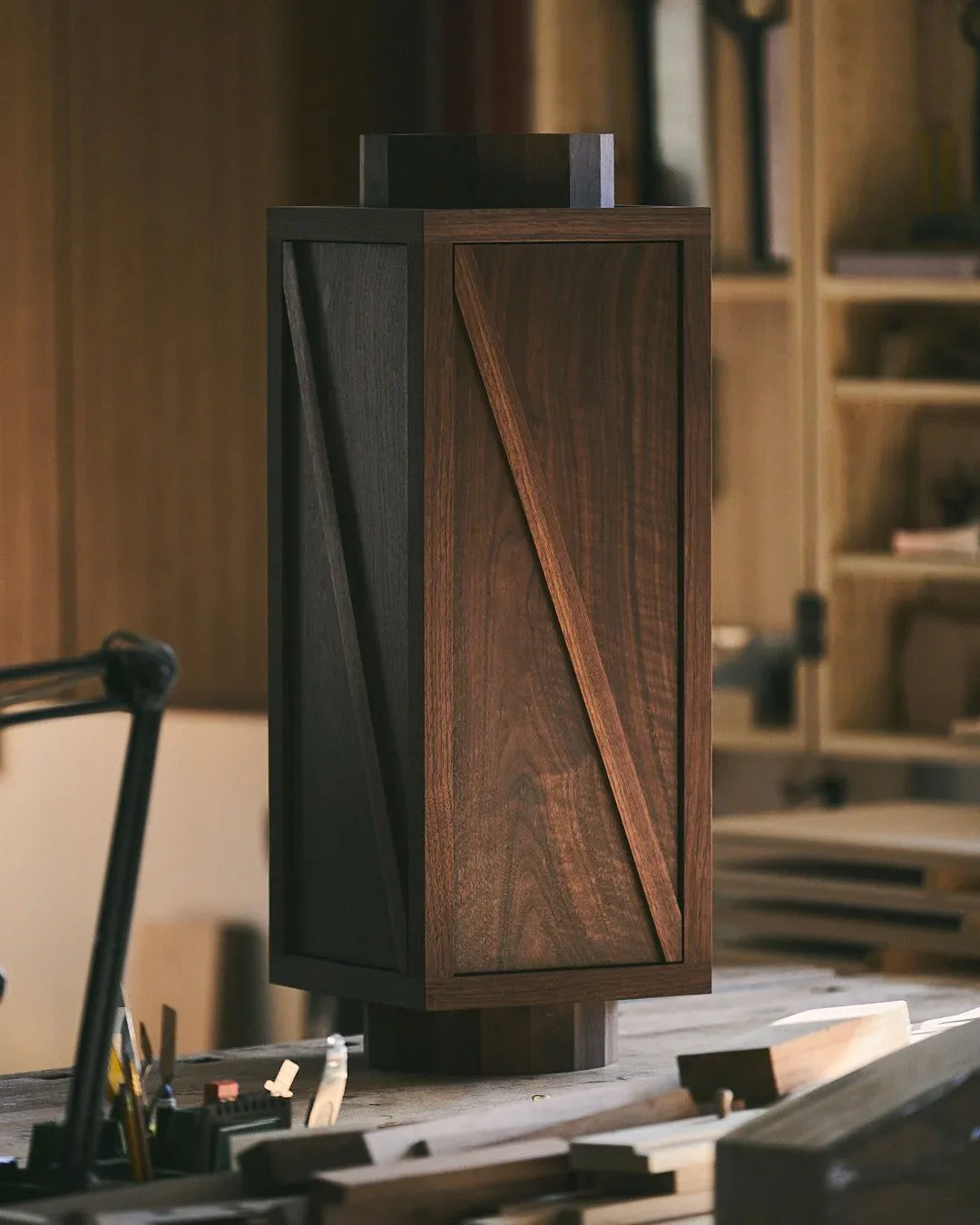 Dark wood speaker cabinet with geometric panel detailing on a desk in a warm-toned interior, designed by Maren Jevremov.