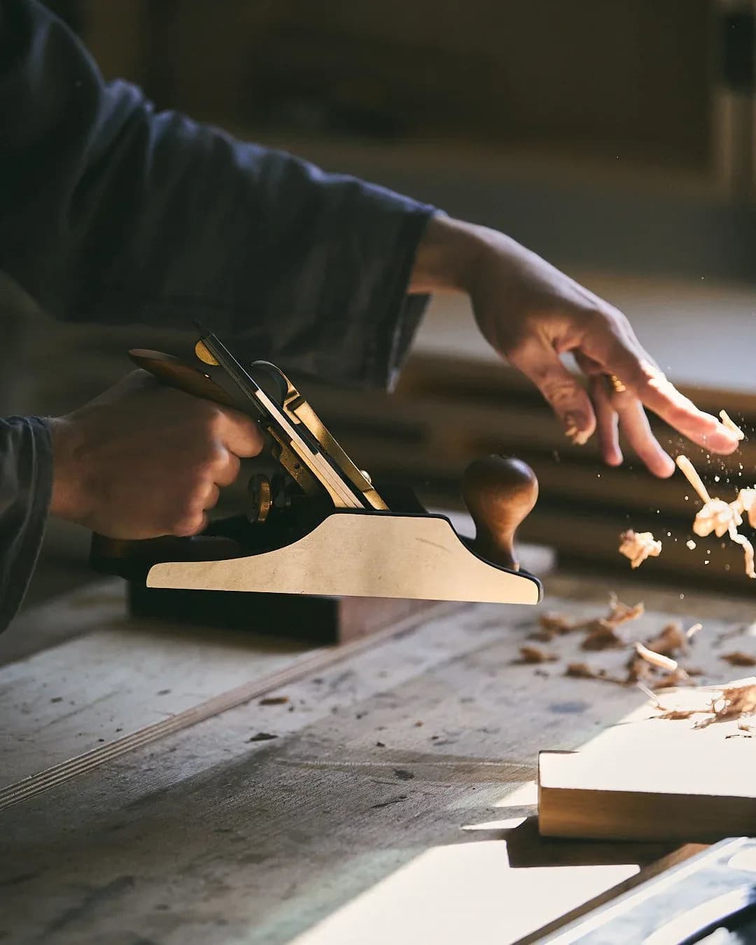 Woodworker's hands planing a wooden board on a work surface, showing craftsmanship and detail in carpentry by Maren Jevremov.