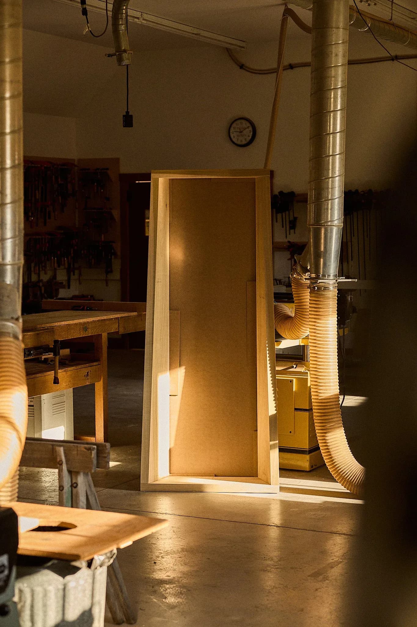 Minimalist wooden interior installation with warm ambient lighting features a tall rectangular panel and industrial ducting elements in a gallery space by Maren Jevremov.