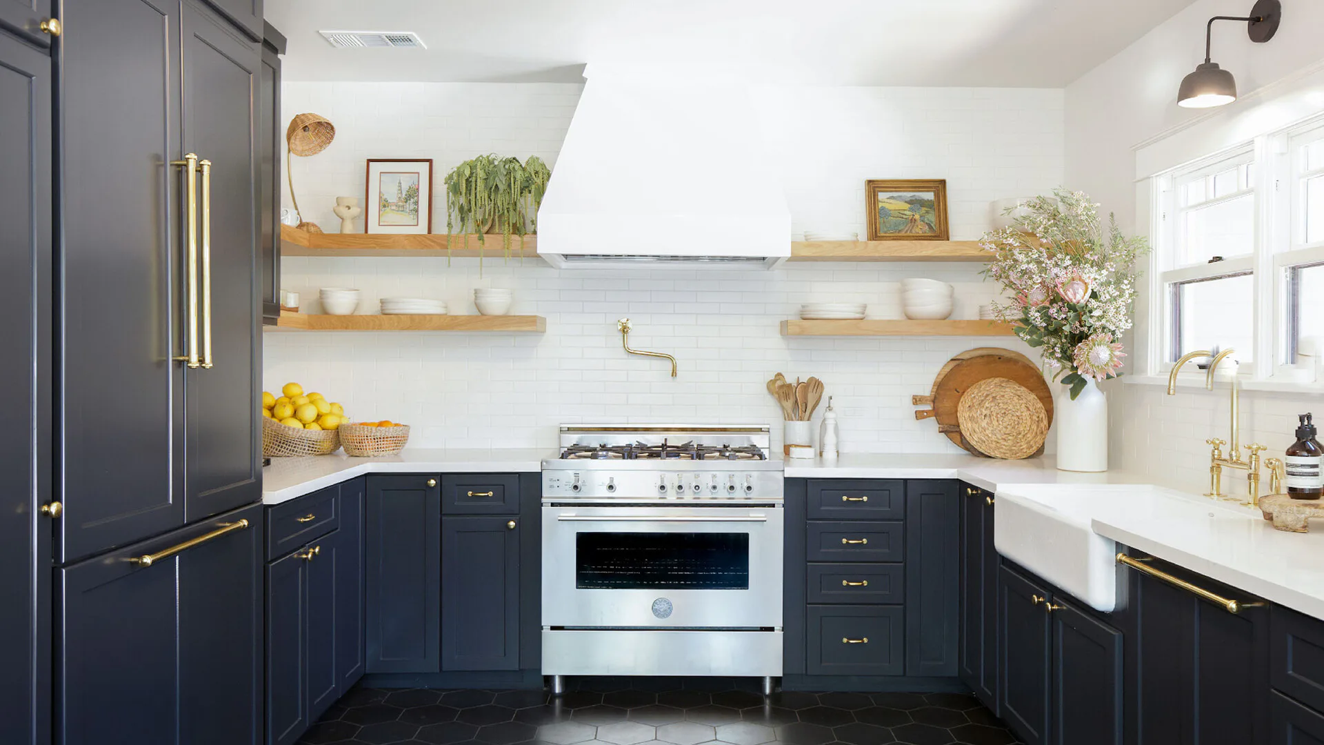 Modern kitchen with dark navy cabinetry, white countertops, open wooden shelving, and a white range hood by Margaret Costello.