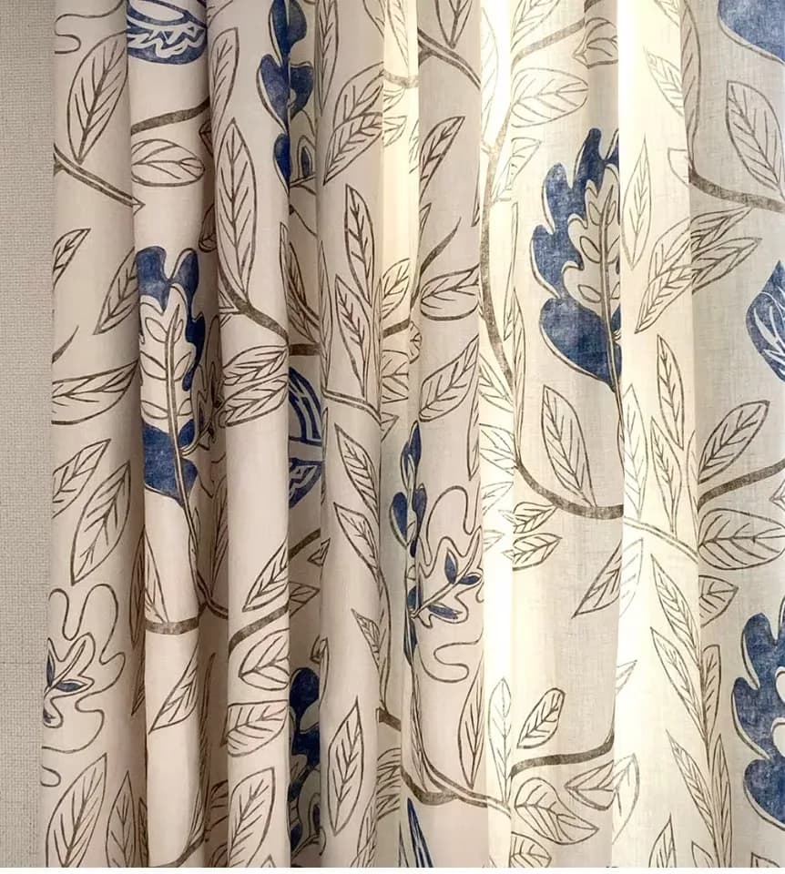 Cream linen curtains with blue and taupe botanical leaf print, hung in generous folds to showcase fabric pattern and draping detail by Margarita Rael.