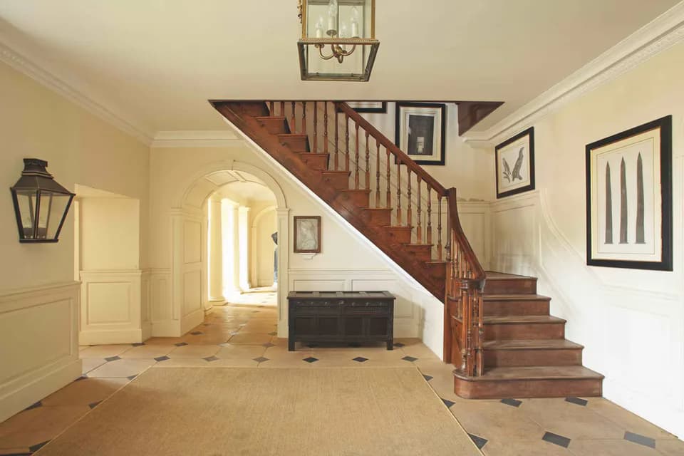 Cream and white foyer with wooden staircase, arched doorway, and geometric floor pattern designed by Maria Filar.